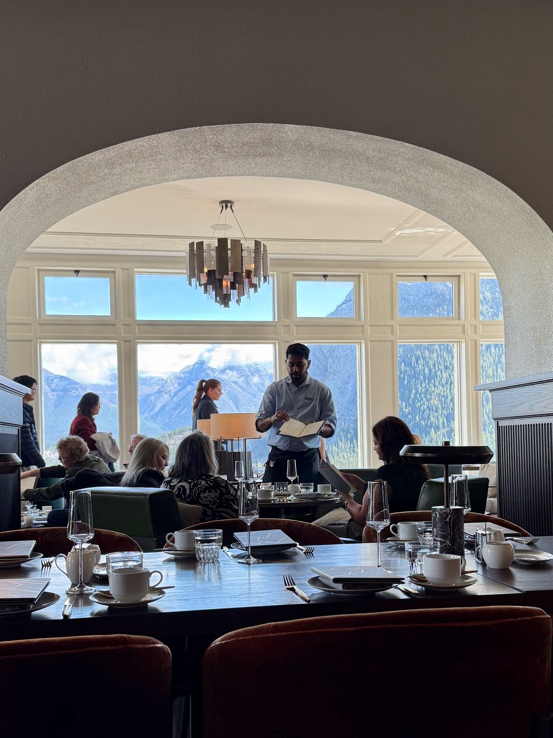 The tea room seen through a stone arch, tables laid in front of tall windows filled with mountains