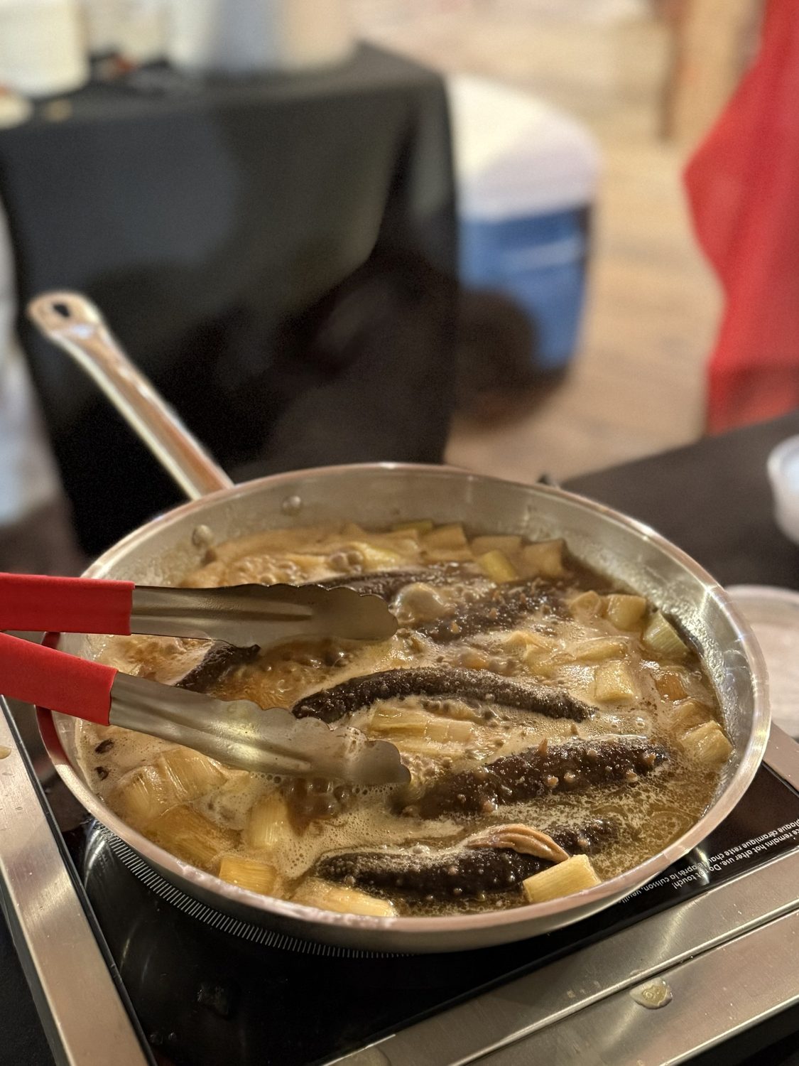 Whole sea cucumbers braising with scallions in a stainless pan on an induction burner