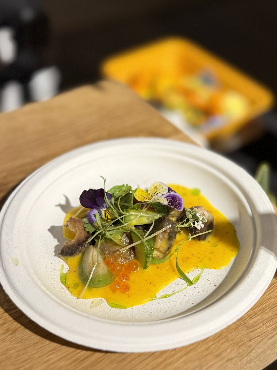 Seared sea cucumber in a bright yellow ají amarillo emulsion with ikura, green oil, violas and microgreens