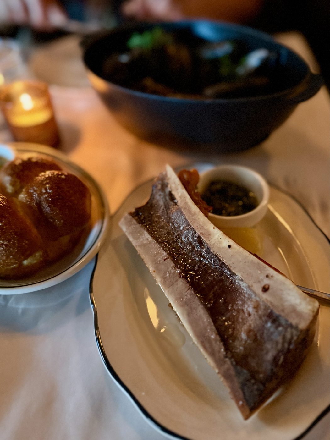 A single split roasted marrow bone, salted and glossy, with a narrow spoon and a ramekin of salsa verde alongside