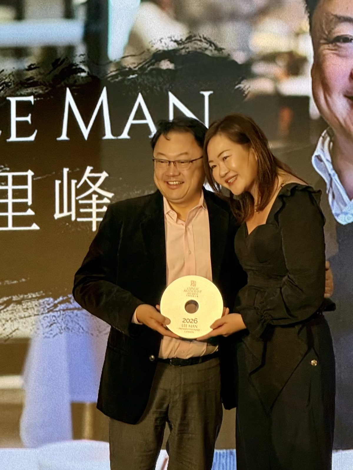 An honouree receiving a round award on stage in front of a large screen