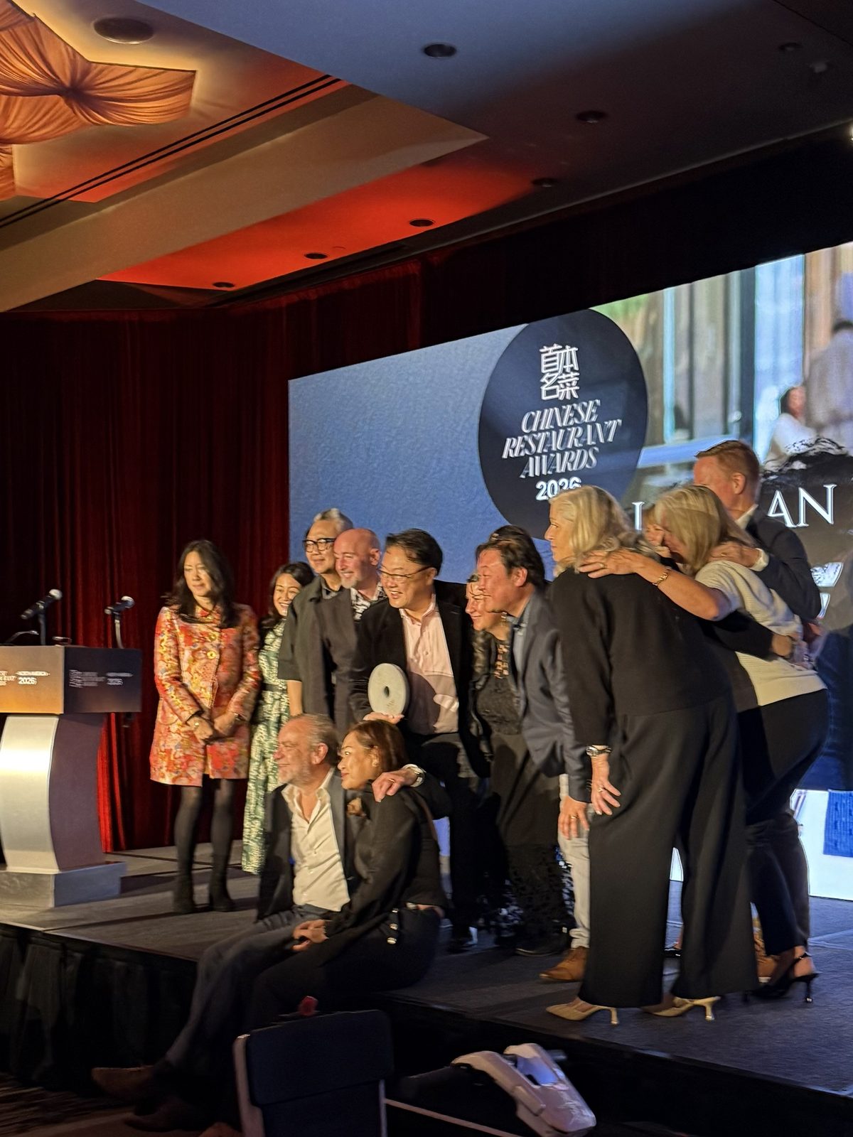 An honouree holding a round award, surrounded by family and friends on stage