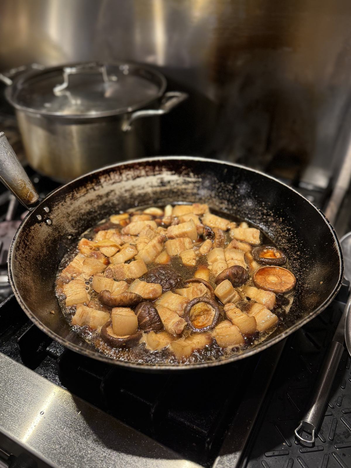 Pork belly and shiitake in dark braising liquid coming to the boil in a well-used wok