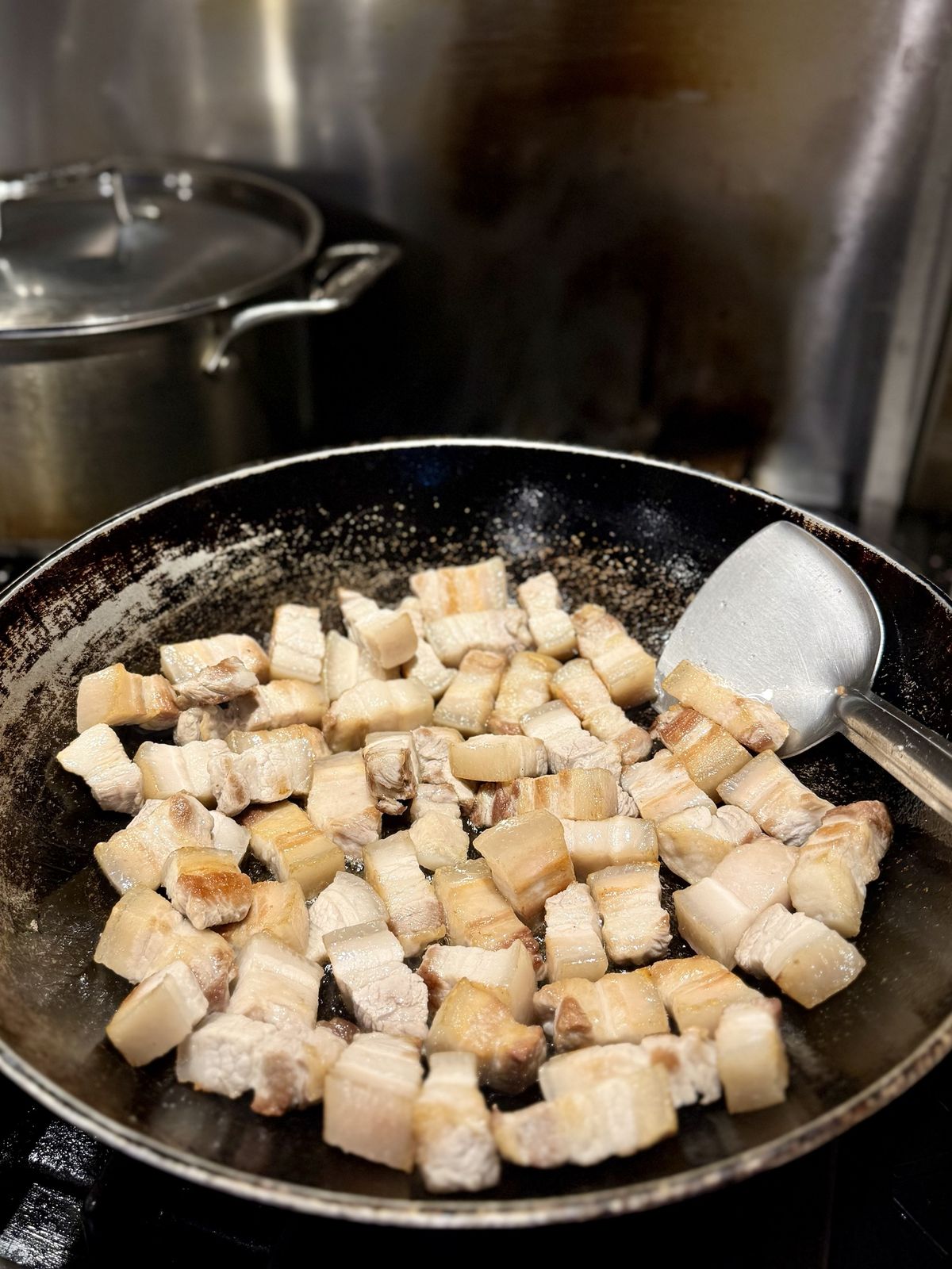 Pork belly pieces spread flat in a wok, turning lightly golden, with a wok spatula