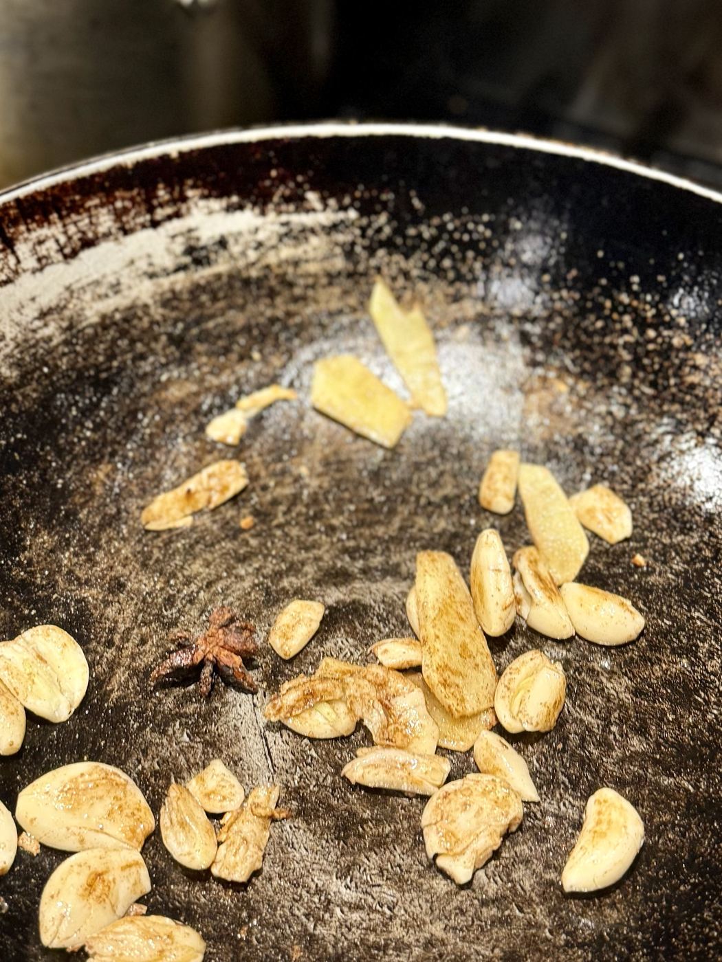 Garlic, ginger slices and a star anise dusted with five-spice in a well-used wok