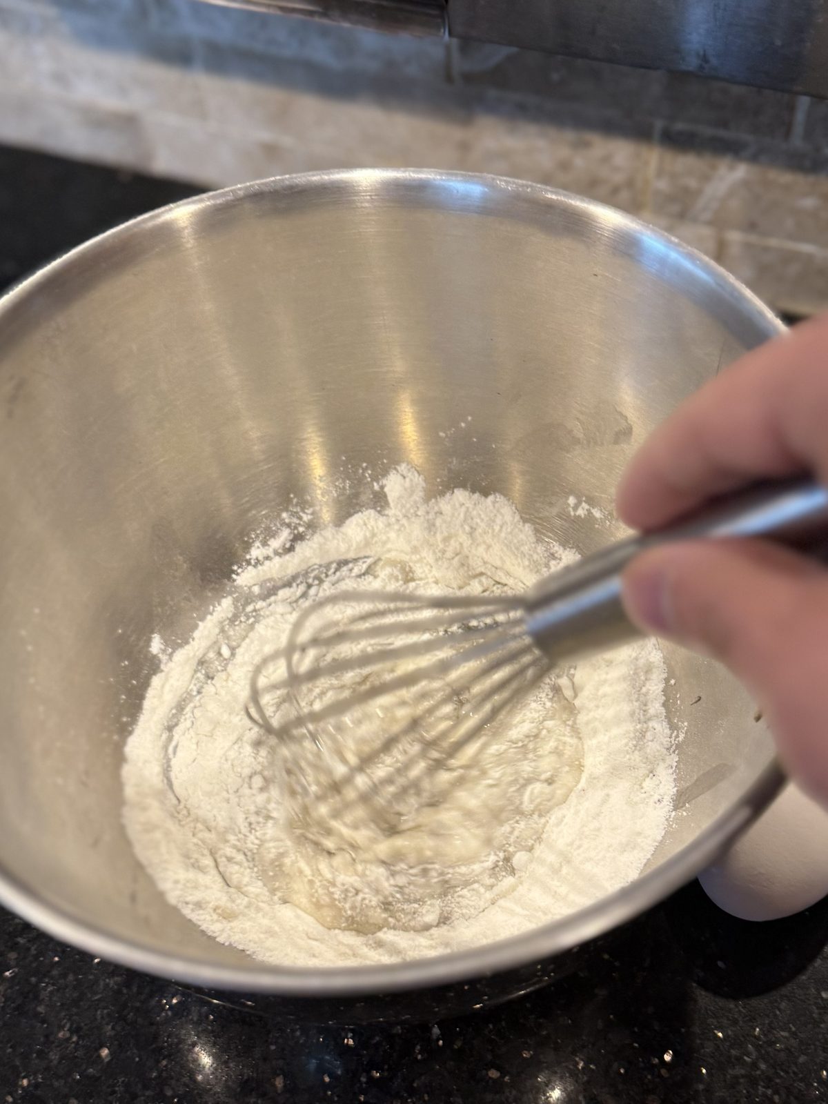 Rice flour and potato starch being whisked with liquid in a steel bowl
