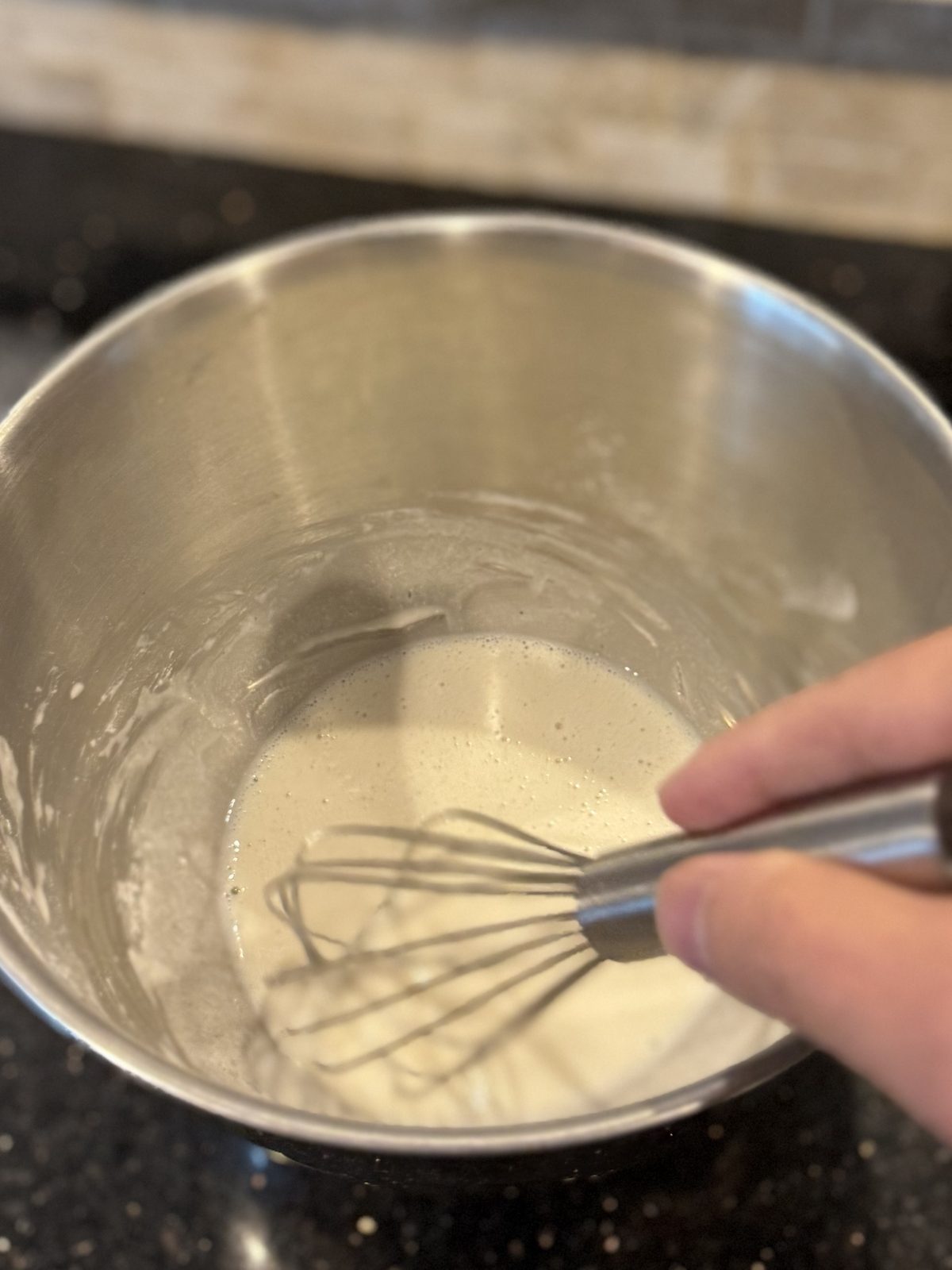 Smooth, pale batter in a steel bowl with a whisk