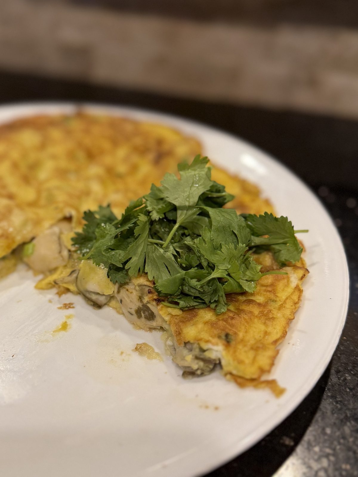 The oyster omelette cut open on a white plate, whole oysters visible inside, cilantro heaped on top