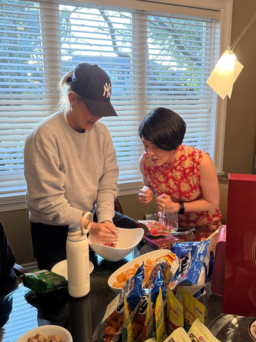 One guest rolls dice into a white bowl while another, in a red qipao, leans in with her fists clenched