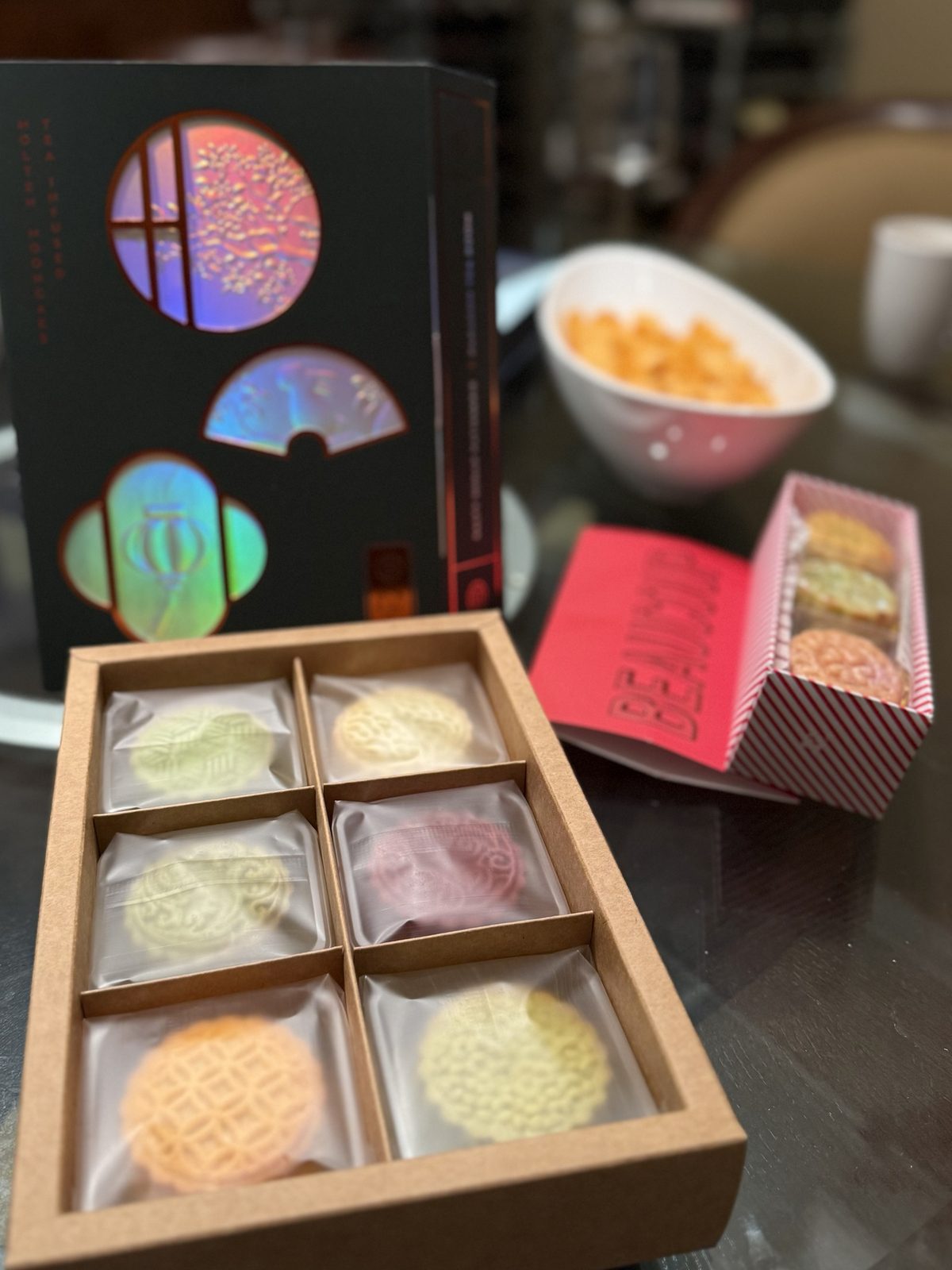 A kraft box of six pastel tea-infused mooncakes in front of a striped box of three more