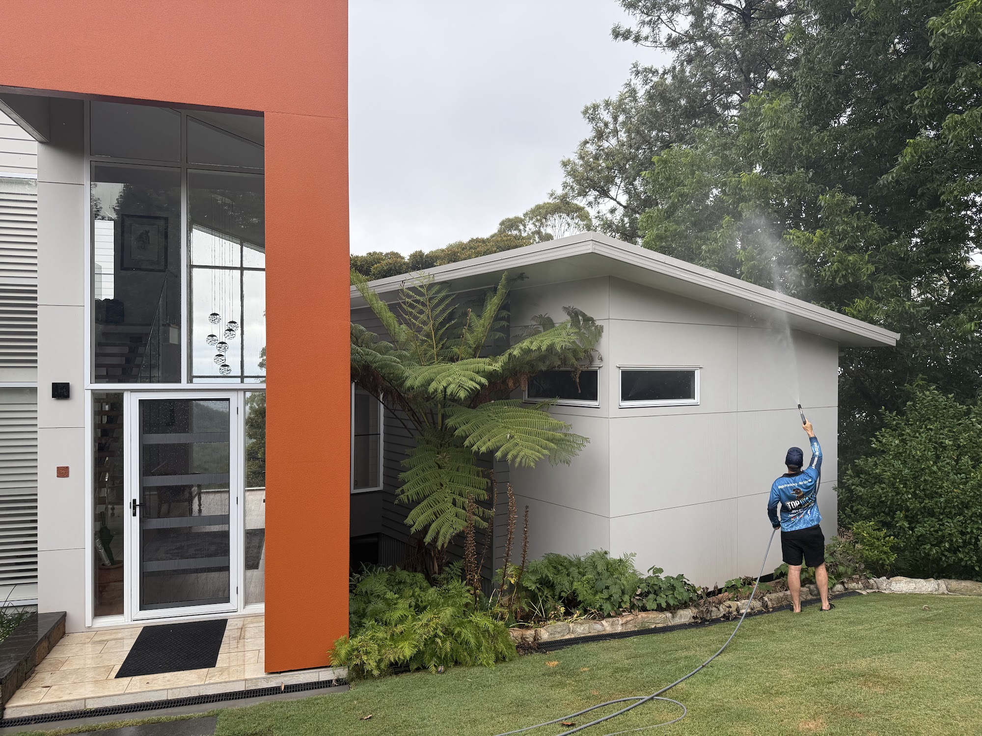 TopWash crew member soft washing the upper wall of a modern Toowoomba home with a telescopic lance