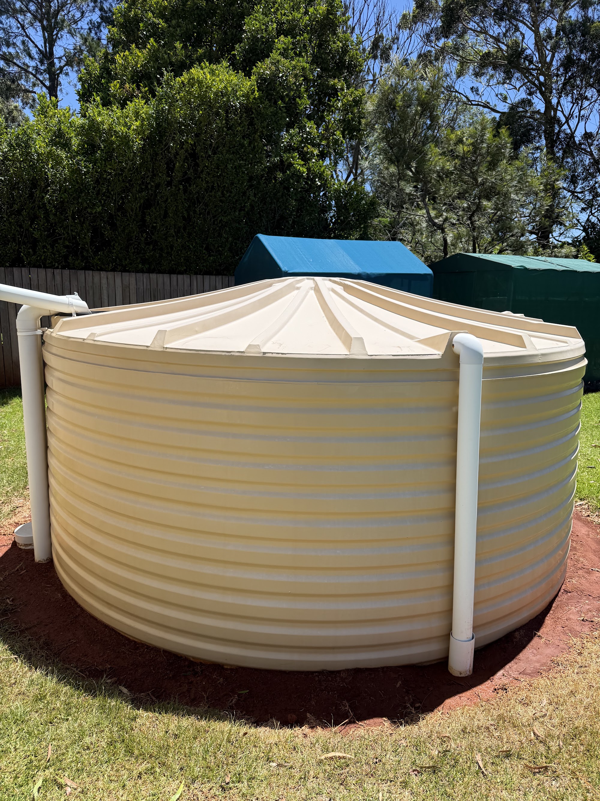 Corrugated rainwater tank cleaned back to cream on its pad in a Toowoomba backyard