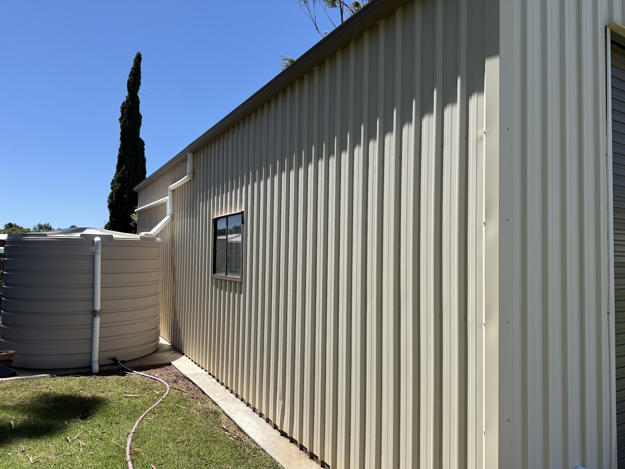 Long cream Colorbond shed wall washed clean, with the rainwater tank at the end