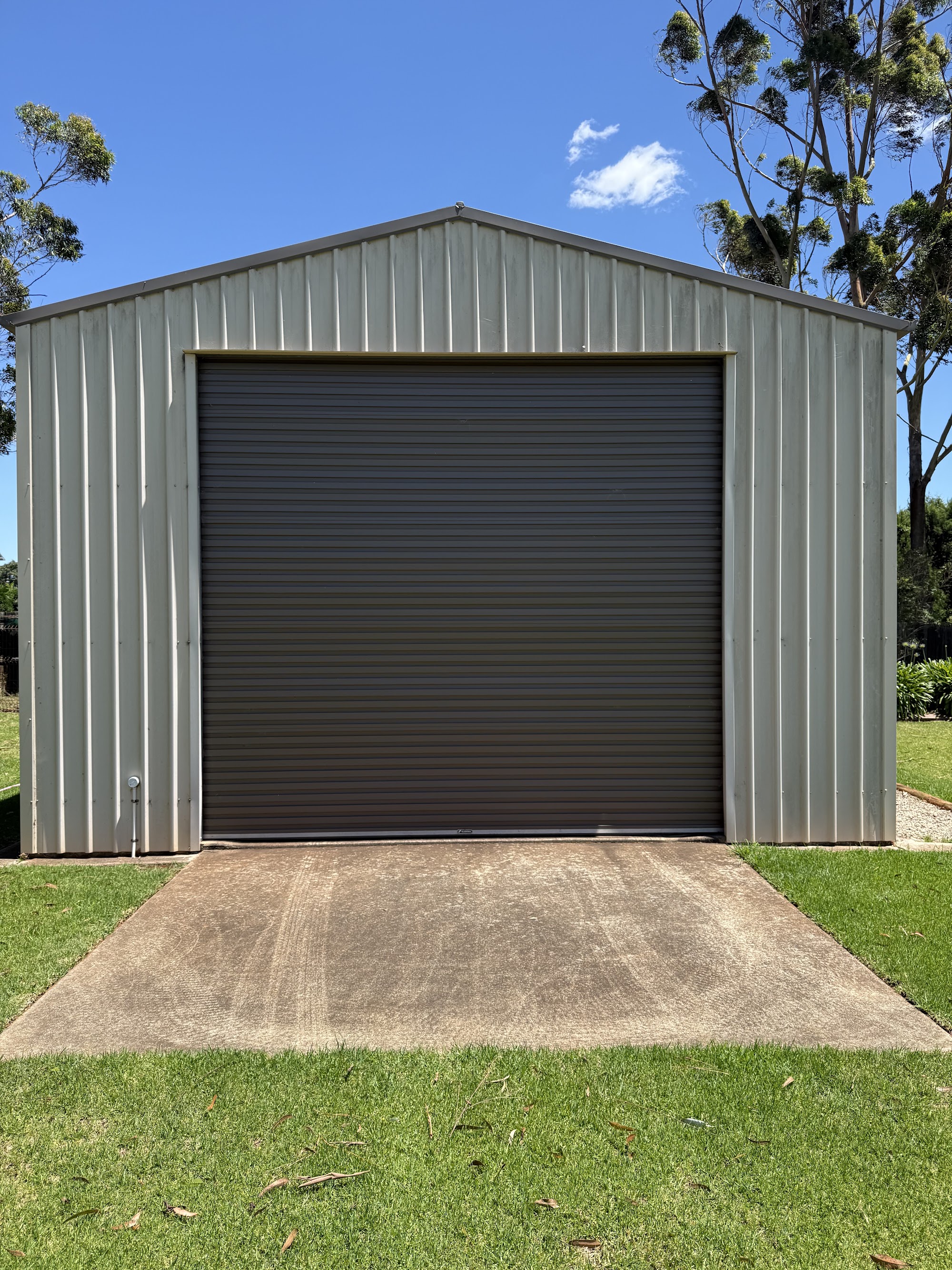 Grey Colorbond shed with a dark roller door, front and apron cleaned