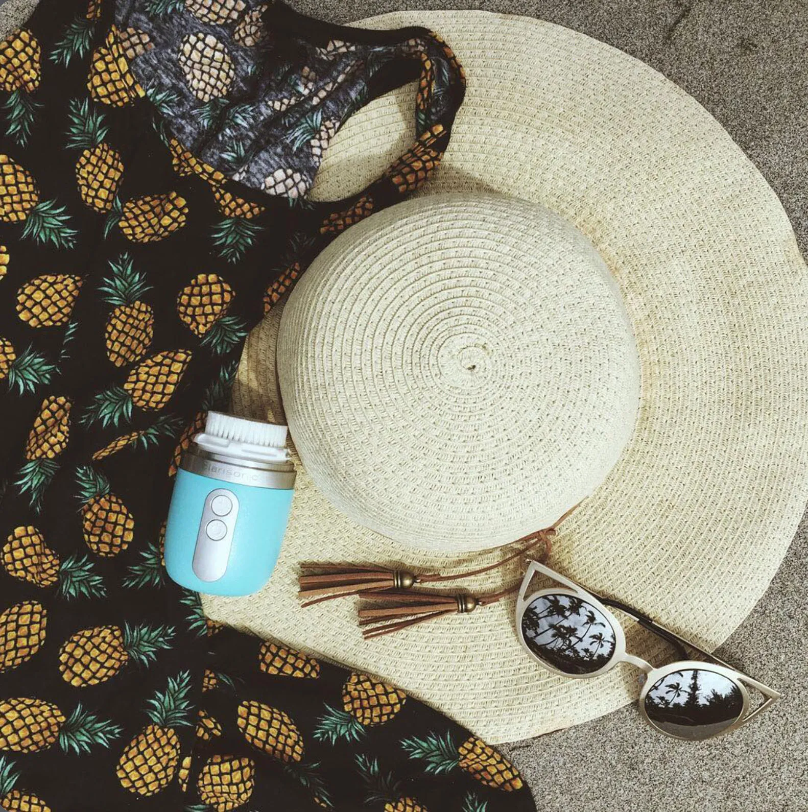 Clarisonic Mia Fit flat lay with straw hat, sunglasses, and pineapple print bag