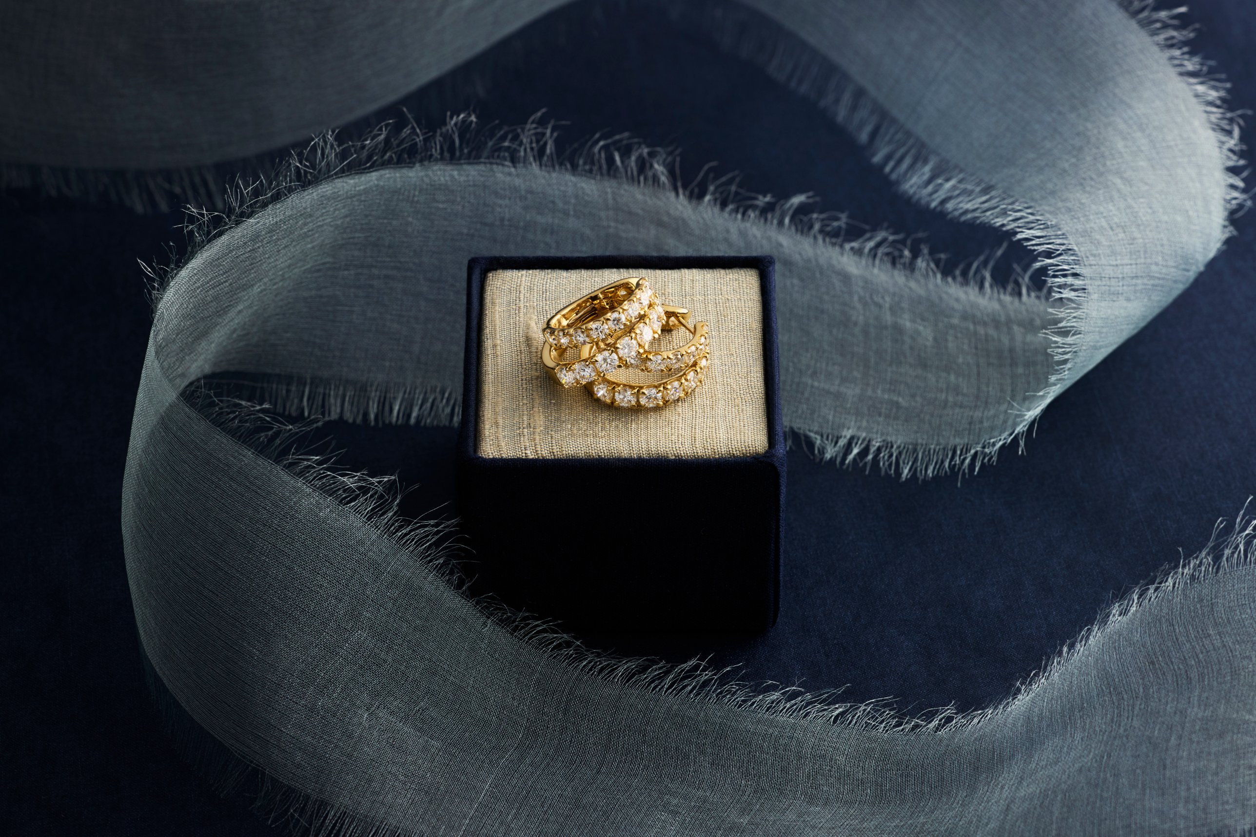 Blue Nile diamond hoops on a navy box wrapped in silk ribbon