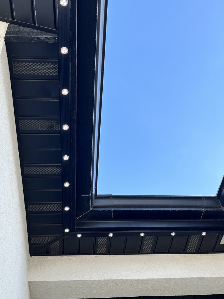 Close-up of permanent lighting nodes installed in a black track beneath a home soffit