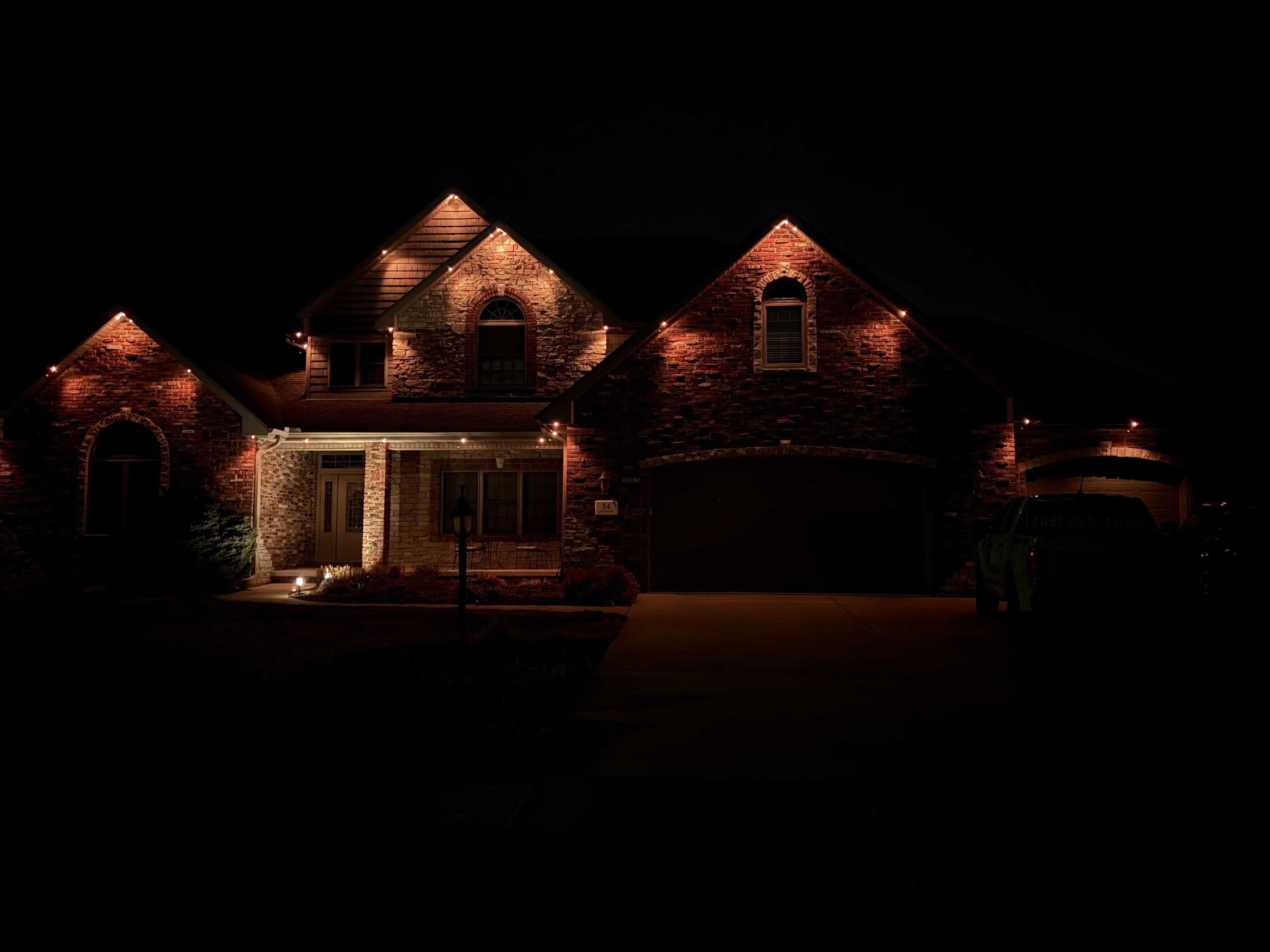 Brick home illuminated with warm amber permanent accent lighting at night