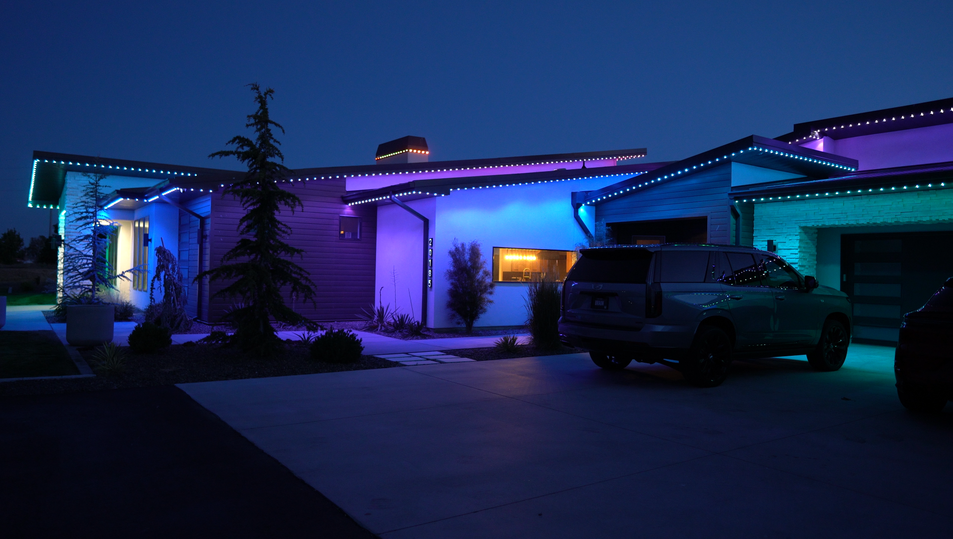 Home illuminated with colorful blue, purple, and teal permanent roofline lighting