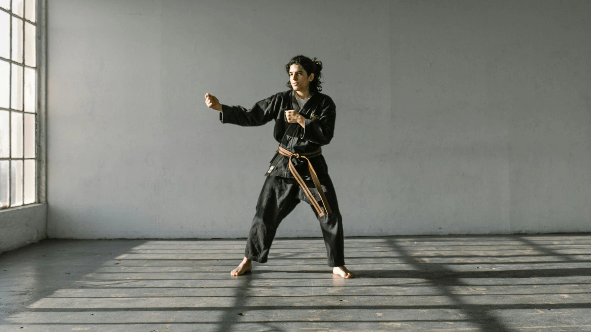 Martial arts student in a black uniform in a ready stance inside a bright dojo