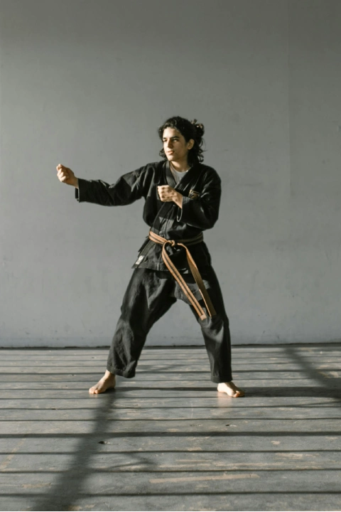 Martial arts student in a black uniform in a ready stance inside a bright dojo