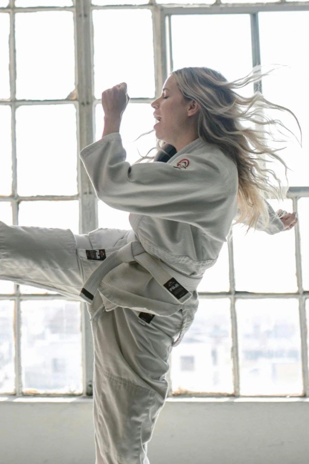 Woman in a white martial arts uniform throwing a front kick into a pad held by her instructor