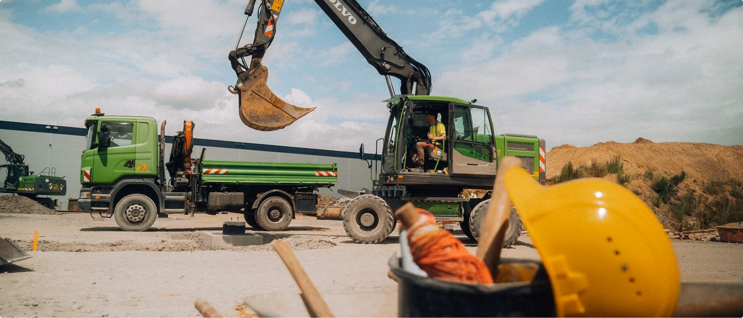 Bagger und Lkw auf einer Tiefbaustelle, im Vordergrund ein Schutzhelm