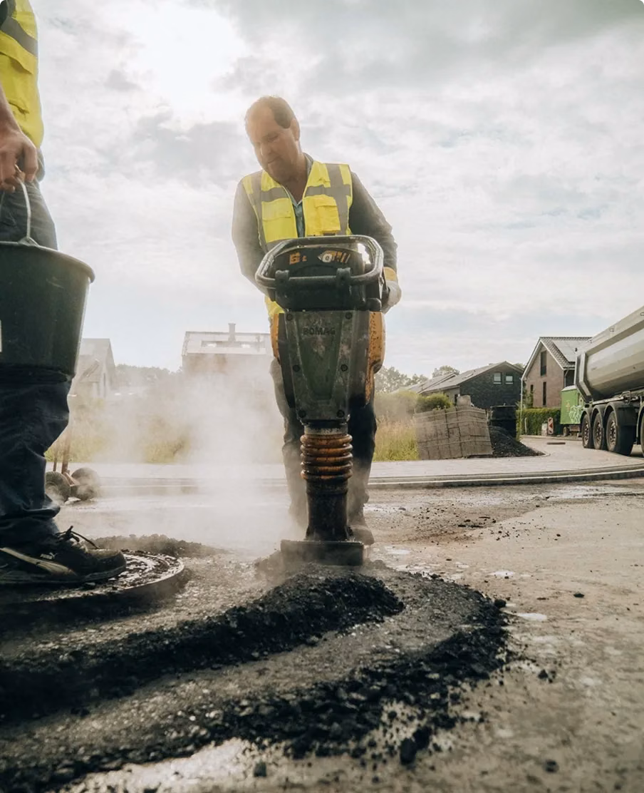Straßenbauer verdichtet frischen Asphalt mit einem Stampfer