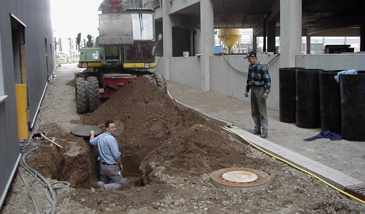 Bogatzki-Baustelle mit Mobilbagger: Ein Mitarbeiter steht lachend in der Baugrube an einem Kanalschacht