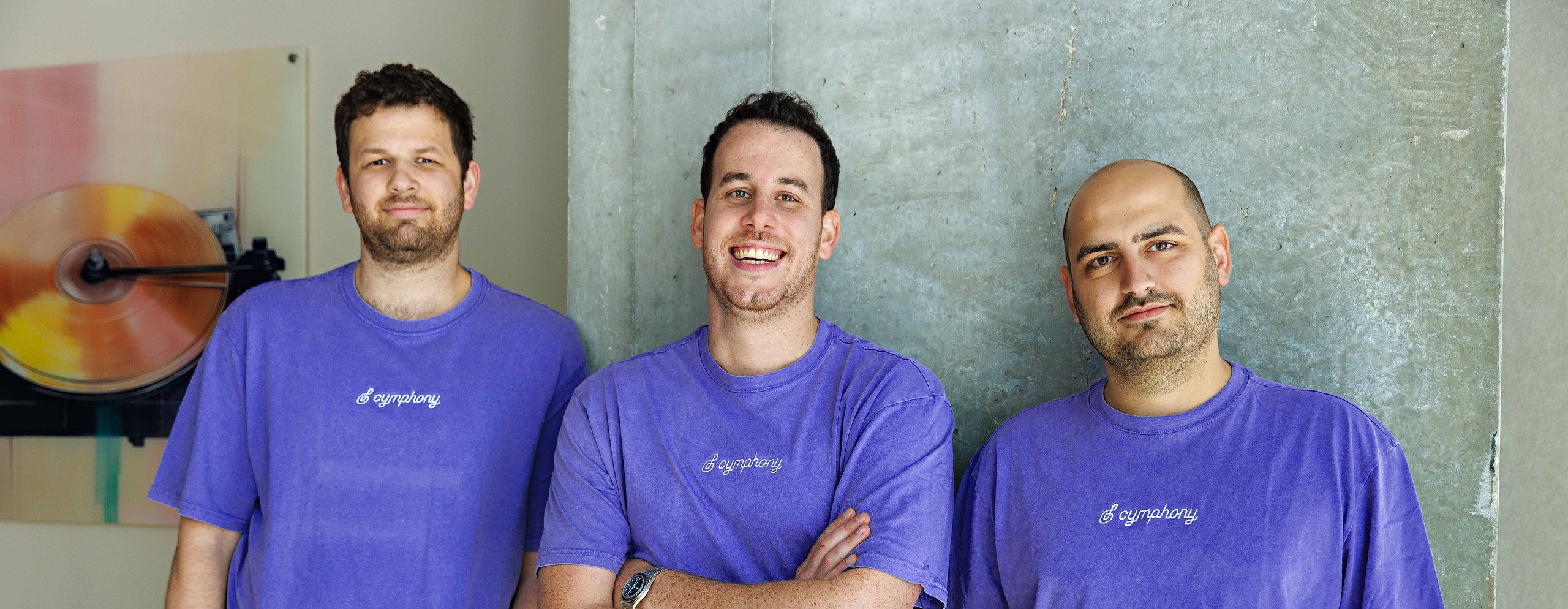 Cymphony’s three founders in purple Cymphony t-shirts against a concrete wall — from left to right, Edi Gotlieb, Shy Dekel and Idan Berkovits.