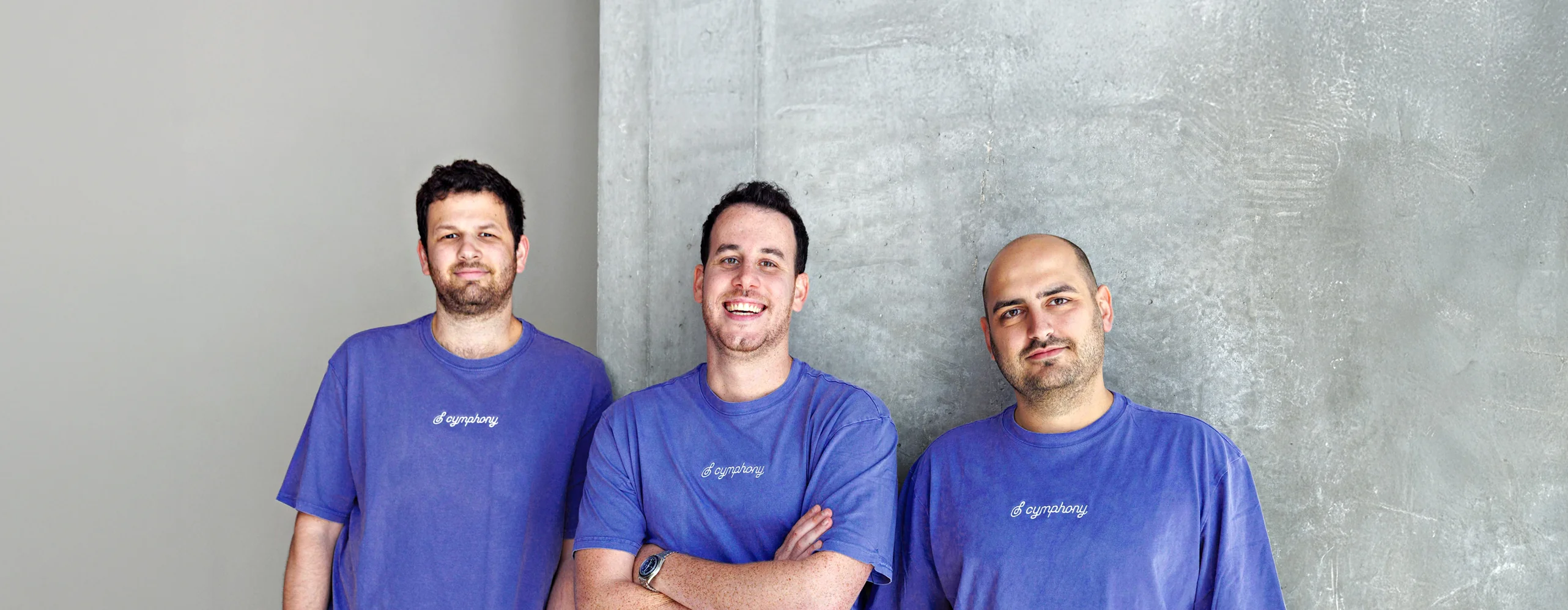 Cymphony's three founders in purple Cymphony t-shirts against a concrete wall — from left to right, Edi Gotlieb, Shy Dekel and Idan Berkovits.