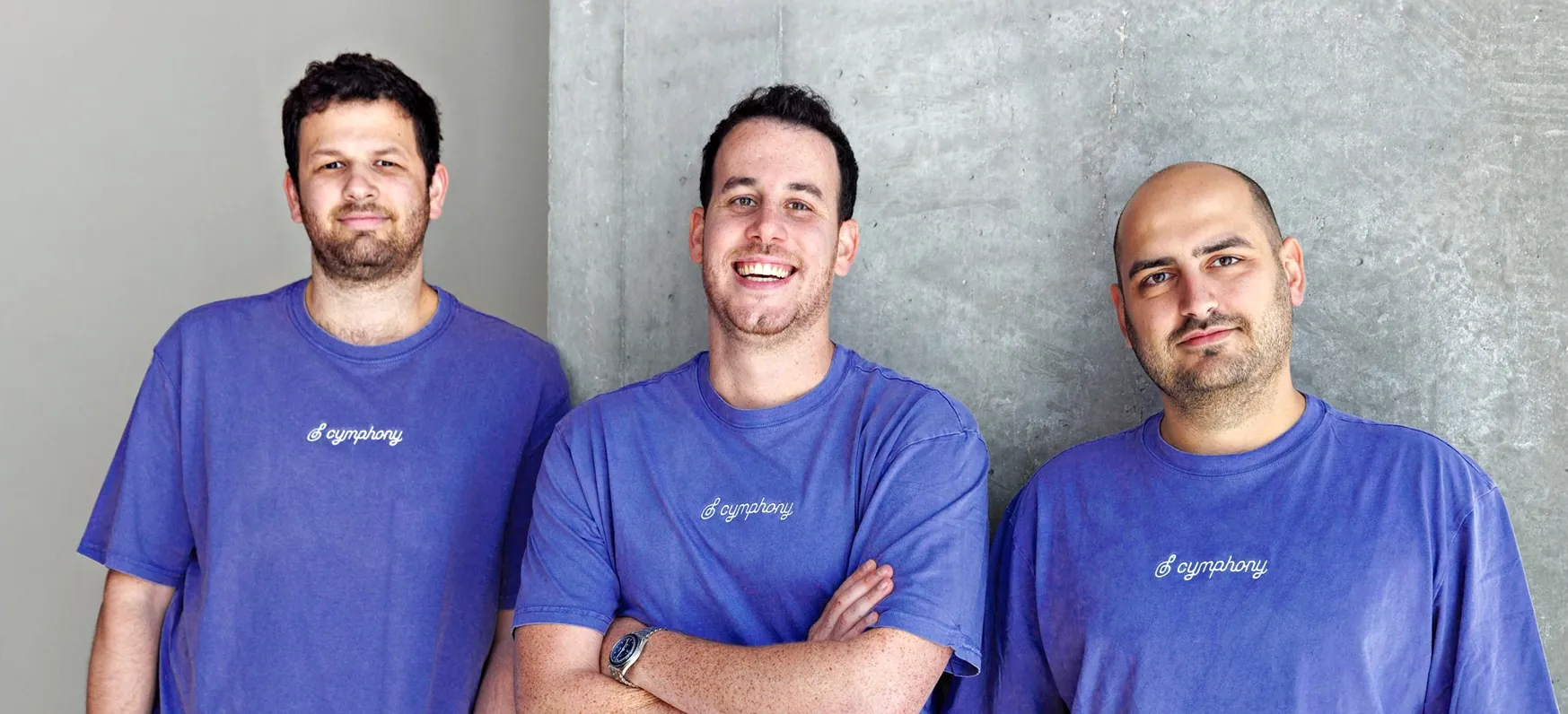 Cymphony's three founders in purple Cymphony t-shirts against a concrete wall — from left to right, Edi Gotlieb, Shy Dekel and Idan Berkovits.