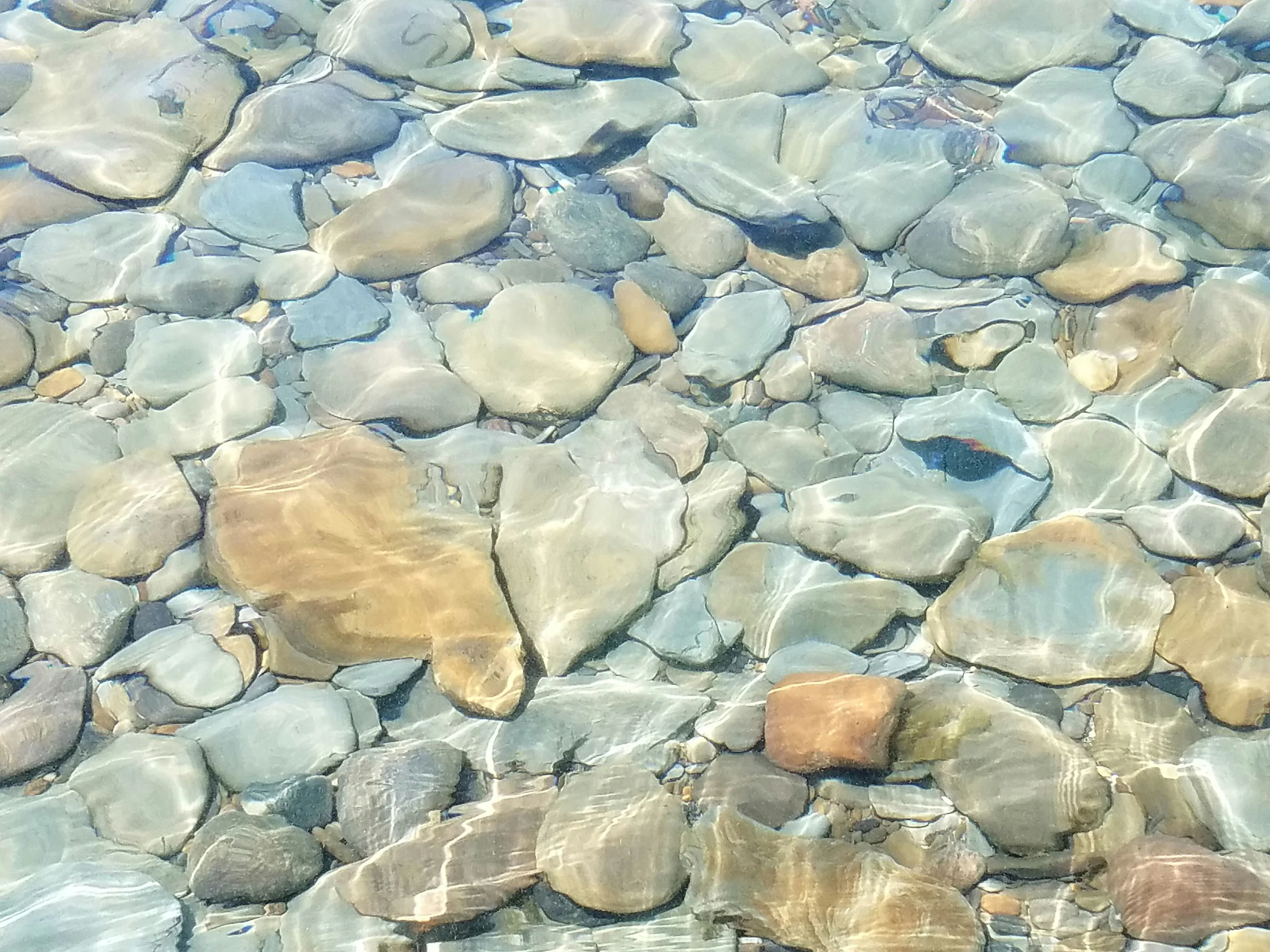 Clear running water over a bed of pale rounded gravel and stones