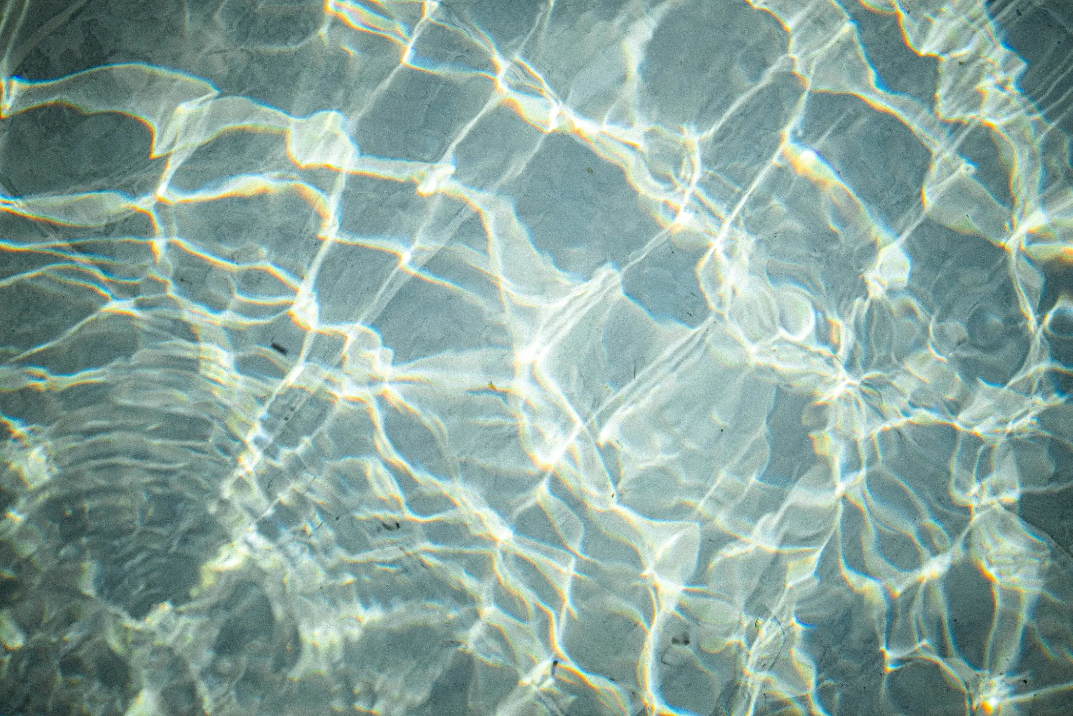 Sunlight refracting through clear shallow water, casting a moving net of light on the bed below