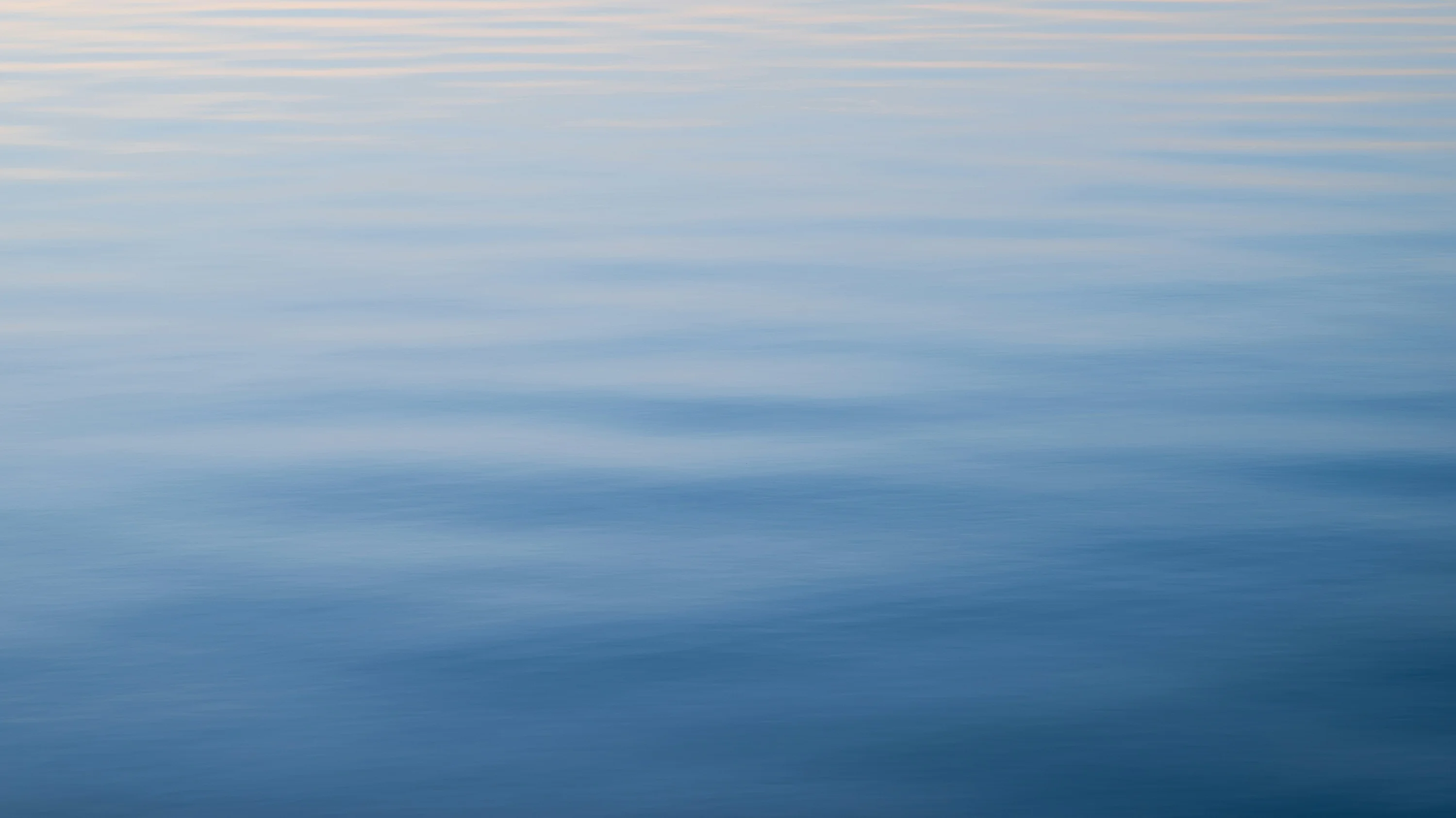 Calm open water at dawn, the surface softly banded in pale blue and silver