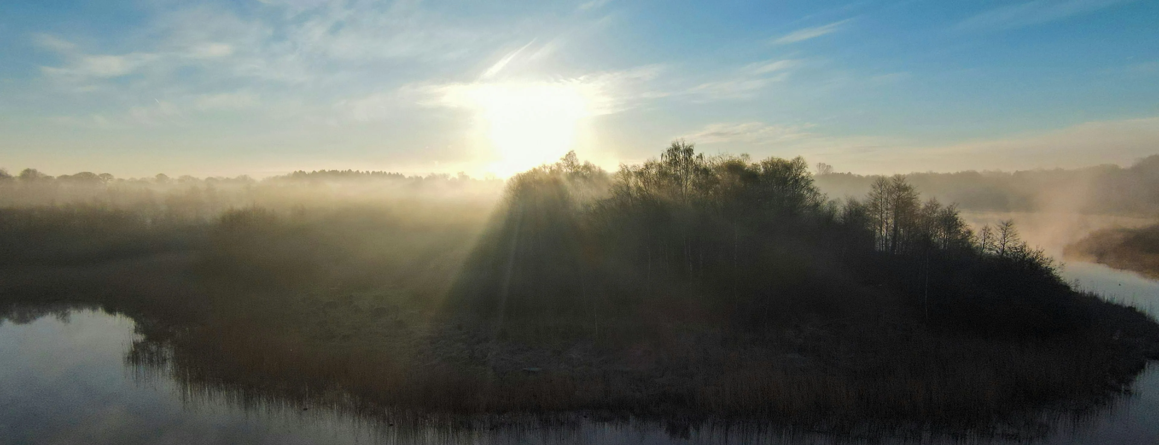 Sunrise burning through morning mist over a lake, the far shore still hidden in fog