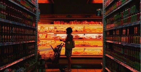 Shopper browsing refrigerated shelves in a warmly lit grocery store aisle