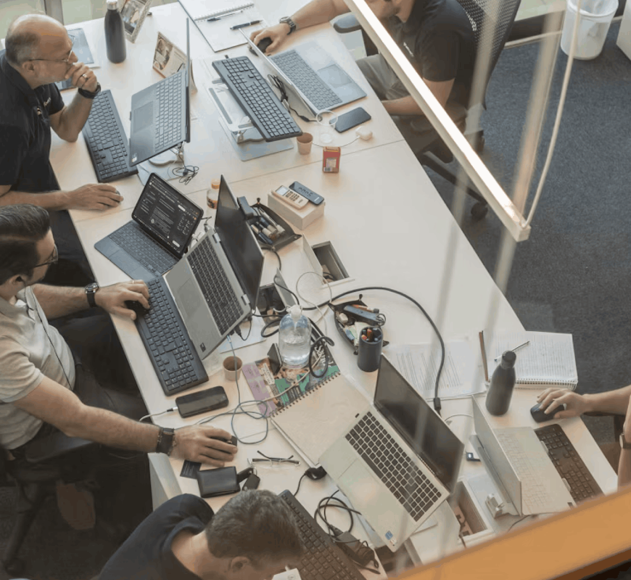 Overhead view of a team working at a shared desk with multiple laptops in an open office.