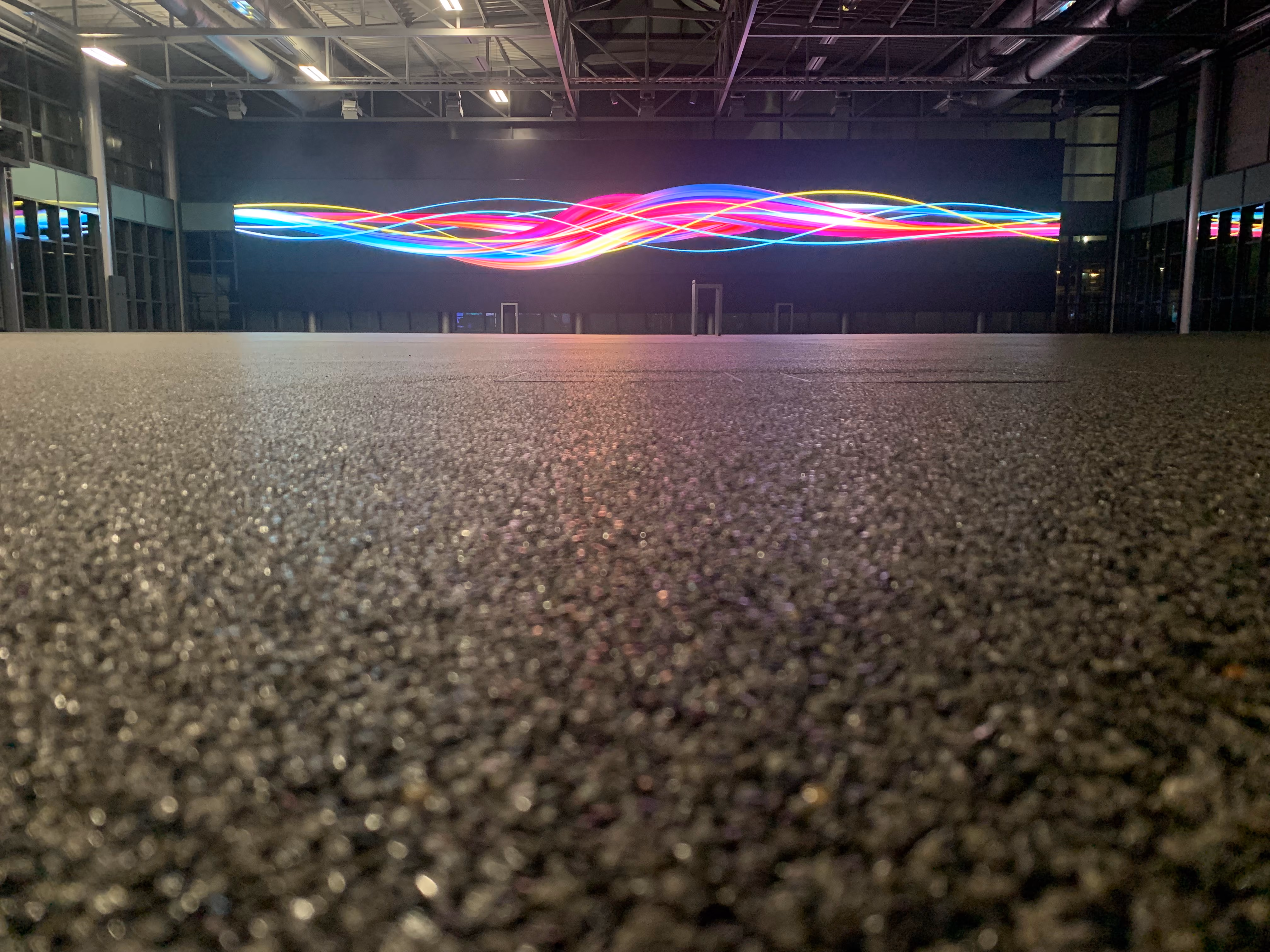 Industrieraum mit strukturierter Steinteppich-Bodenfläche und leuchtender LED-Wand mit bunten Wellen.