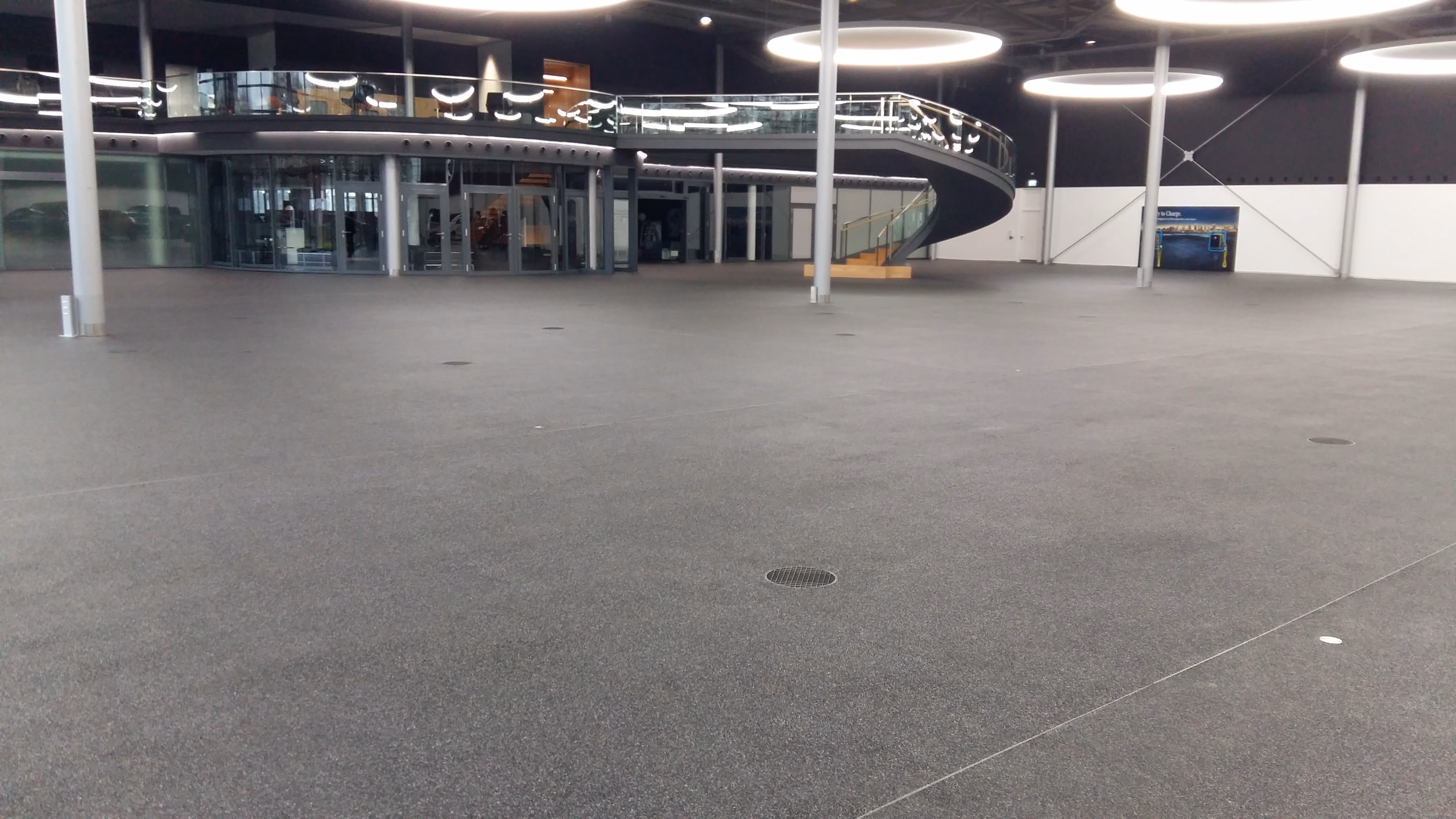 Große leere Halle mit geschwungener Treppe und runden Deckenlichtern in modernem Gebäude.