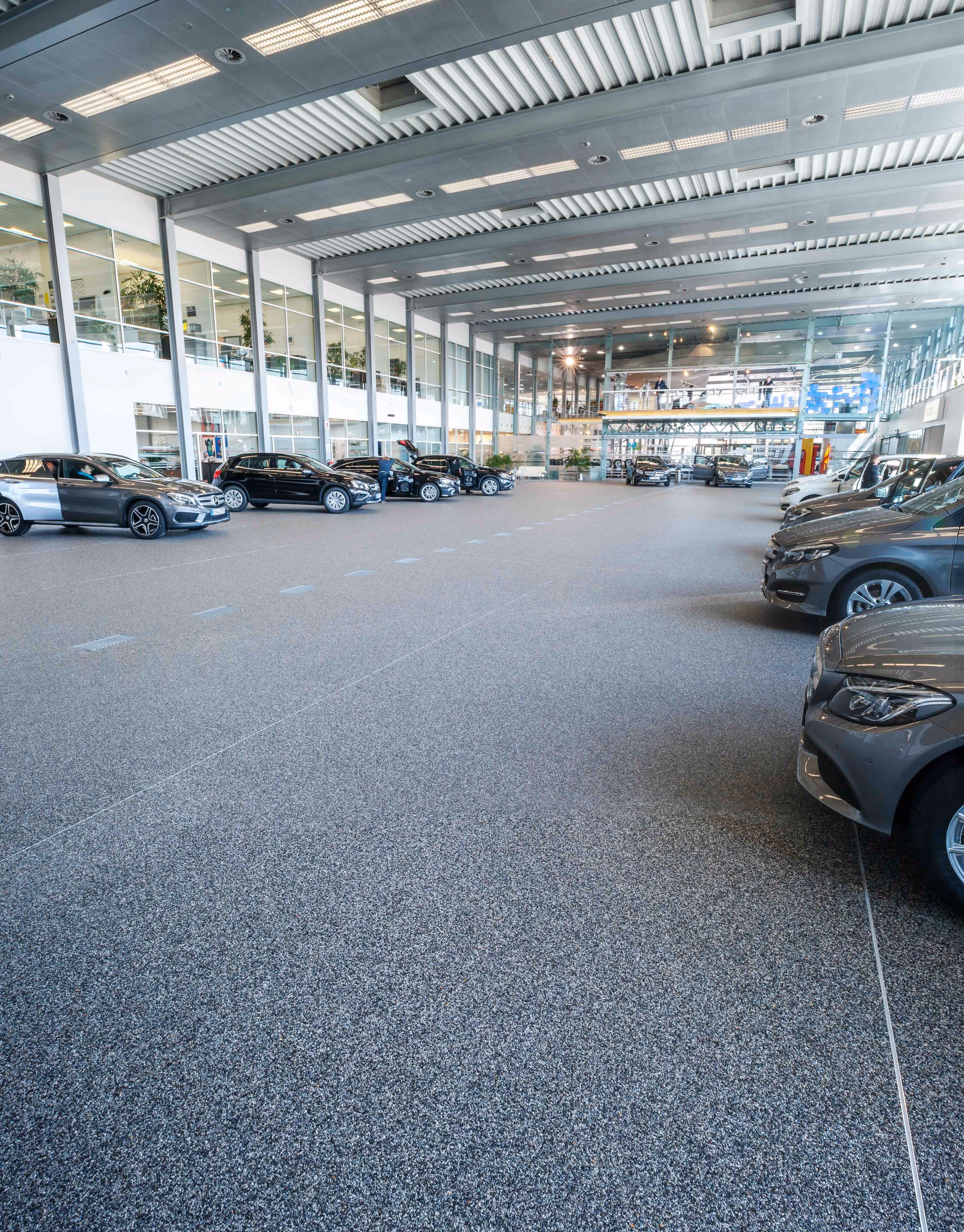 Innenaufnahme eines modernen Autohauses mit mehreren stehenden Fahrzeugen und heller Decke.