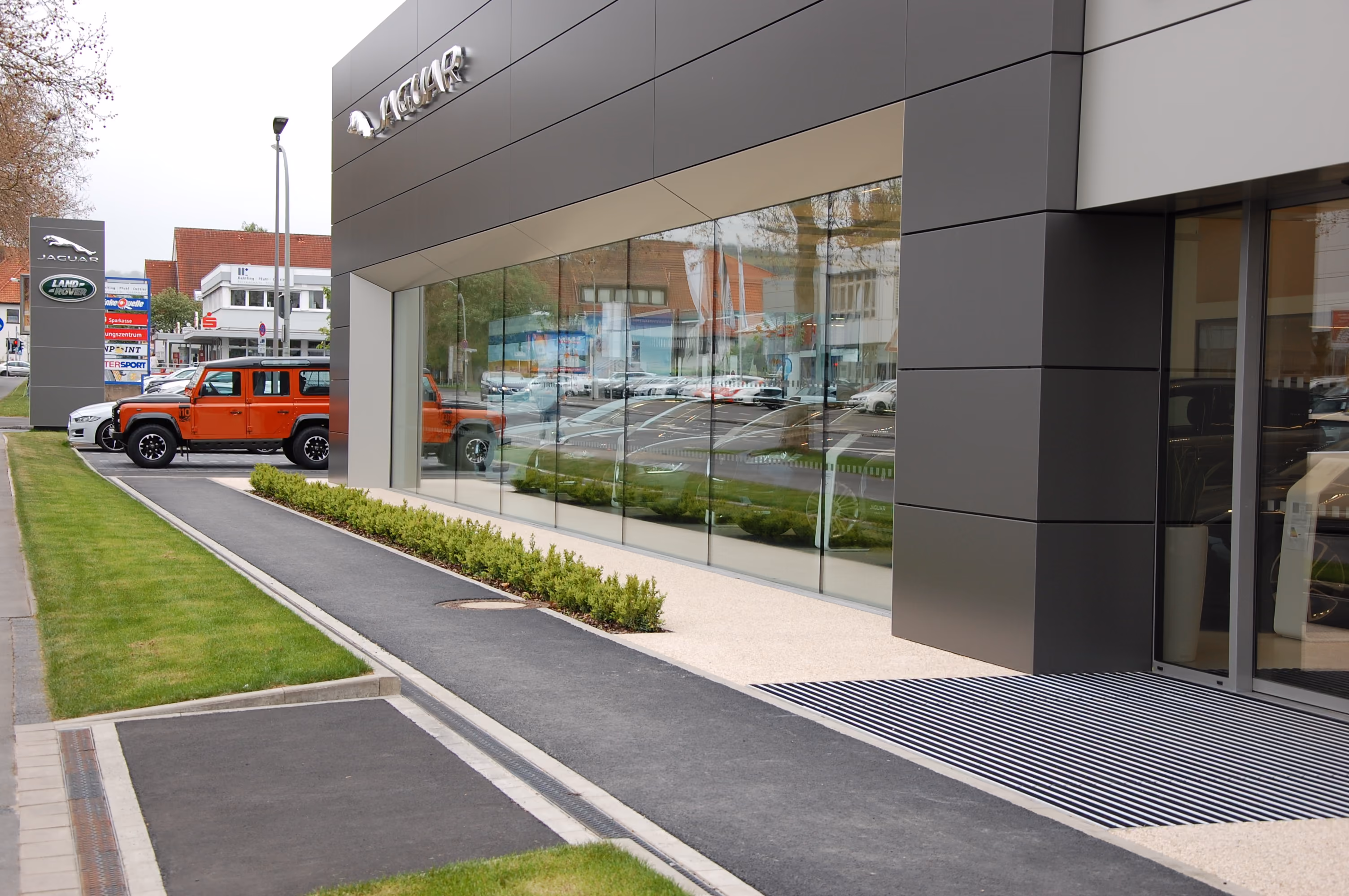 Außenansicht eines Jaguar und Land Rover Autohauses mit roten Fahrzeugen und großem Schaufenster.