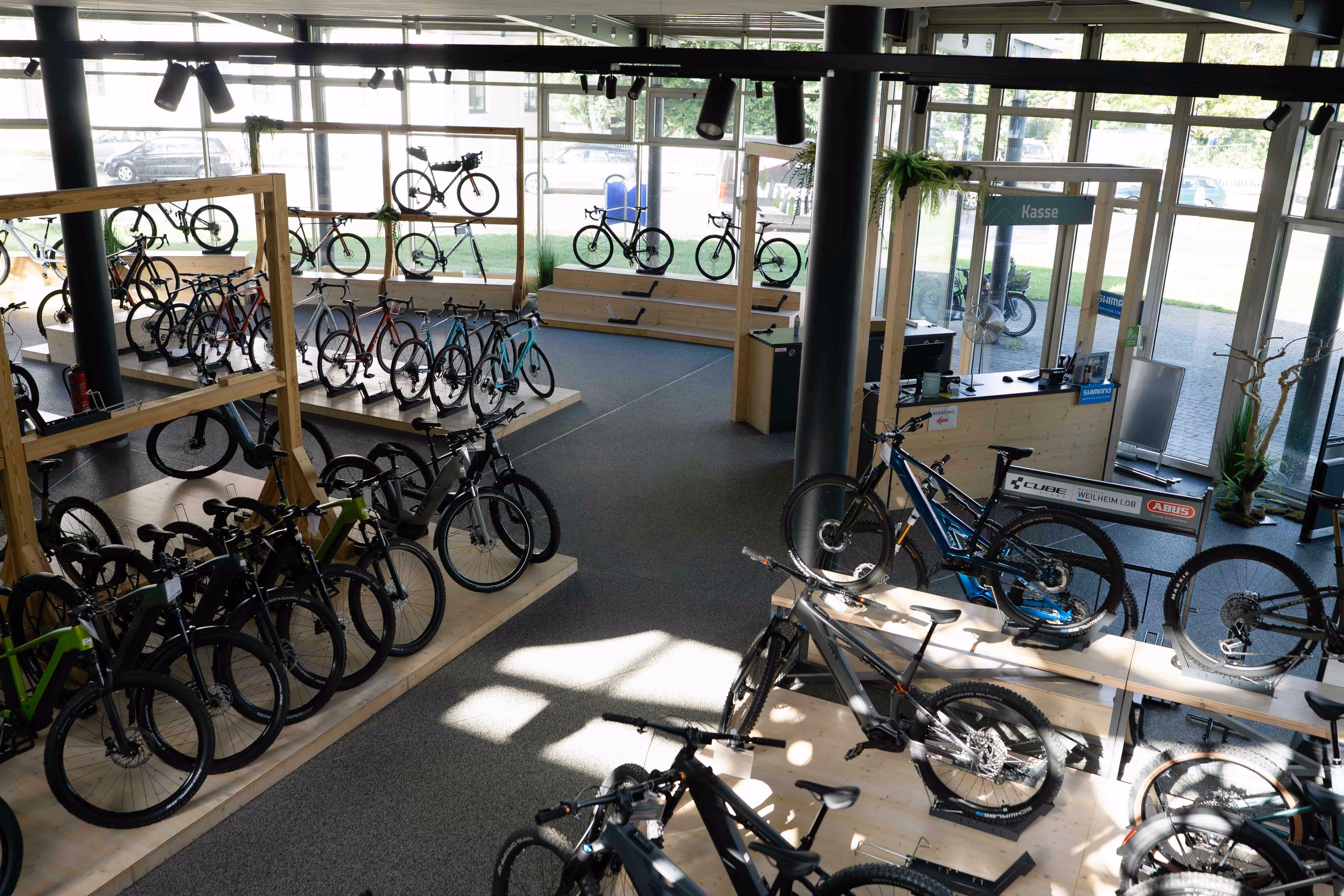 Innenansicht eines Fahrradladens mit vielen ausgestellten Fahrrädern auf Holzständern und großer Fensterfront.