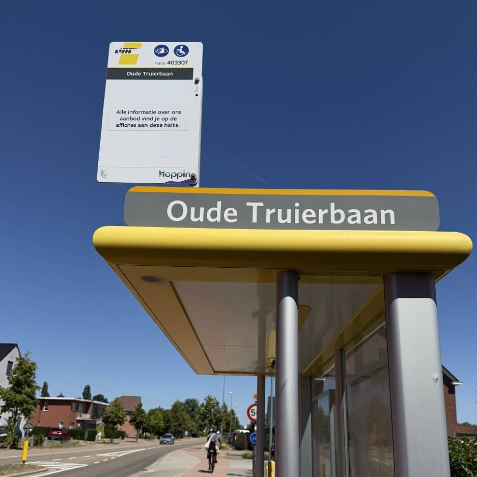Bushalte Oude Truiersbaan met gele overkapping en bord tegen een blauwe lucht, fietser en auto's op de straat in een woonwijk.