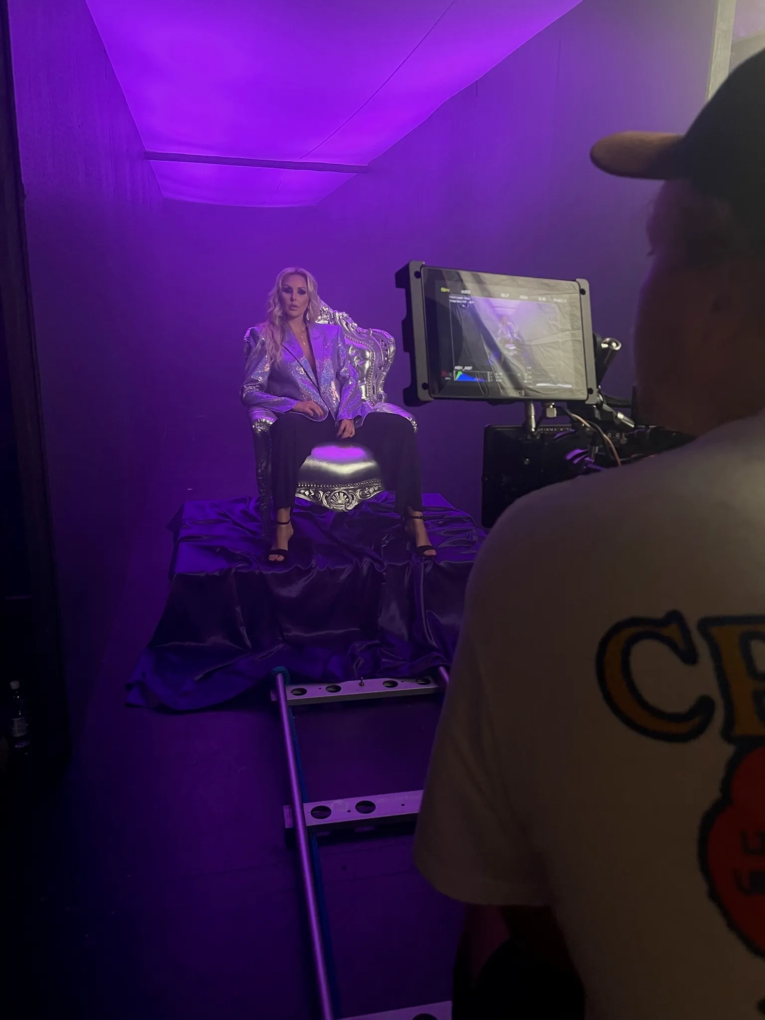 Esiintyjä hopeisessa takissa kameran edessä violetissa studiovalossa.