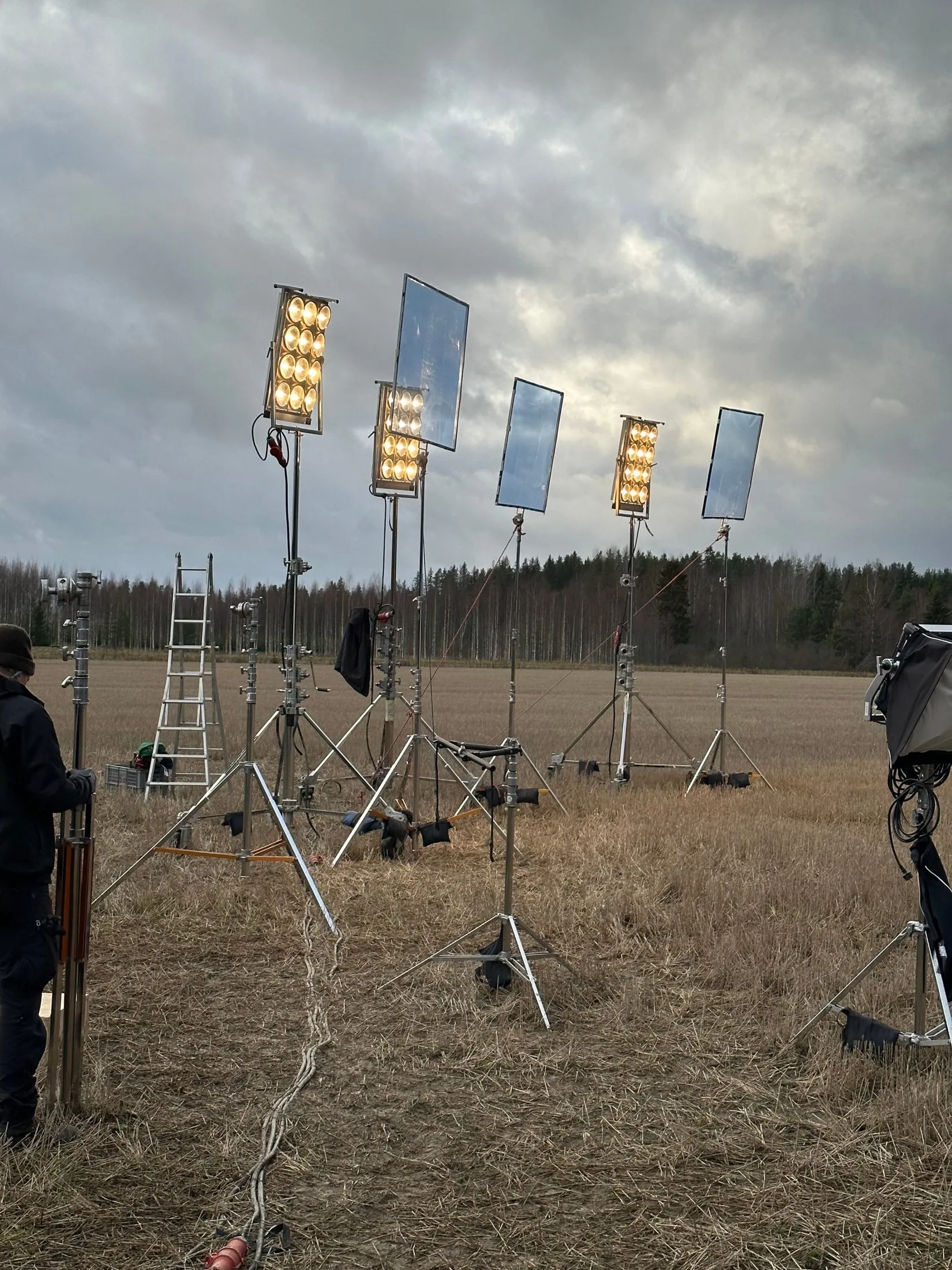 Film lights and reflector panels in a field under a cloudy sky.