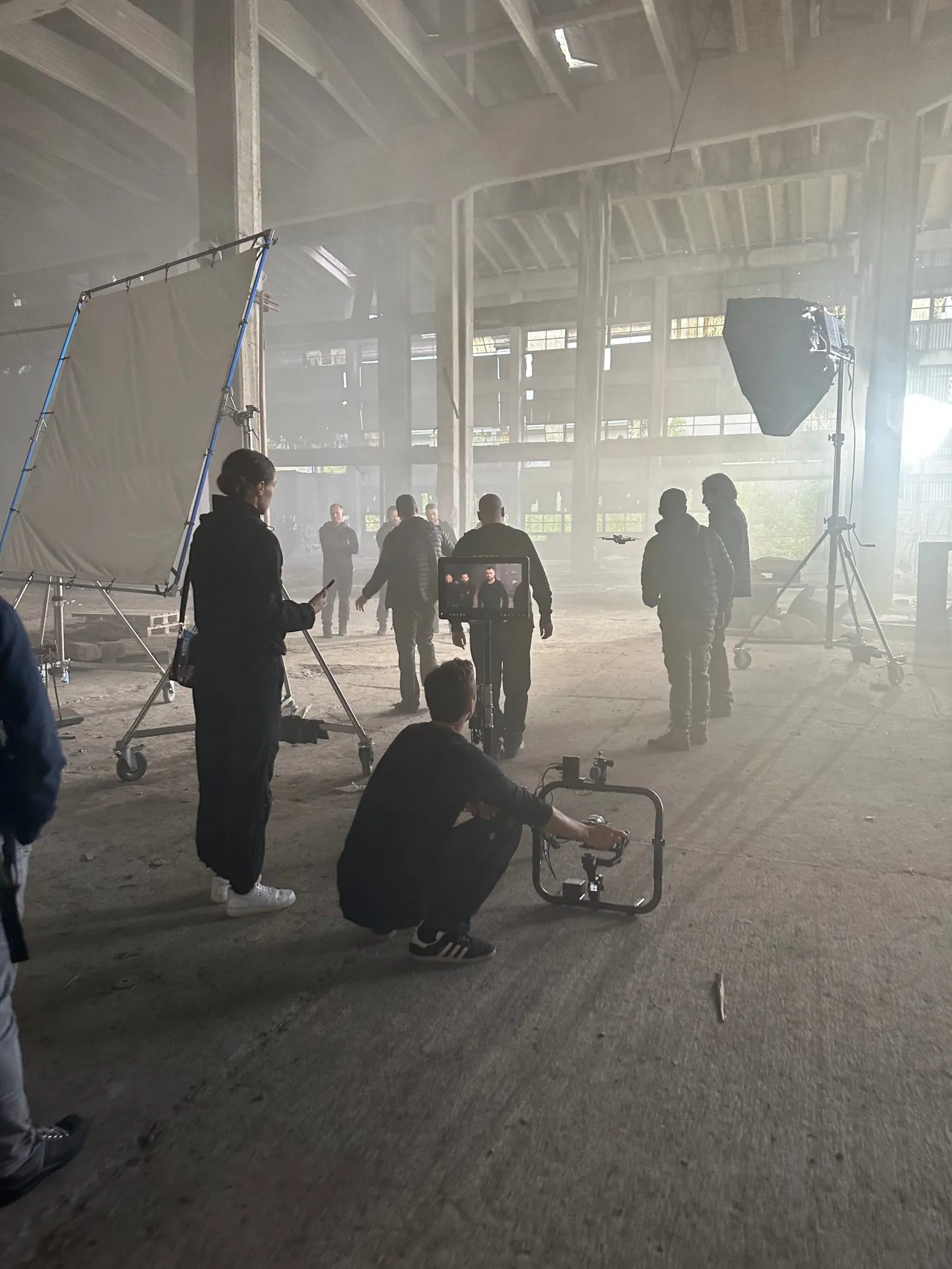 Film crew, camera and lighting equipment in a smoke-filled industrial hall.
