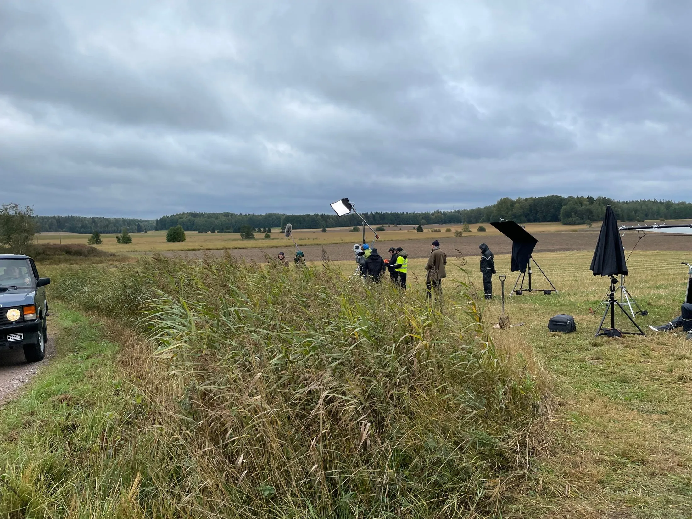Film crew and lighting equipment in a field under a cloudy sky.