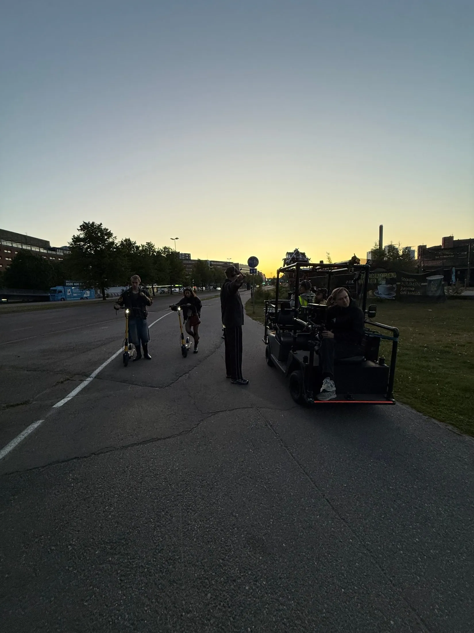 Film crew, camera vehicle and cyclists on a street at summer dusk.