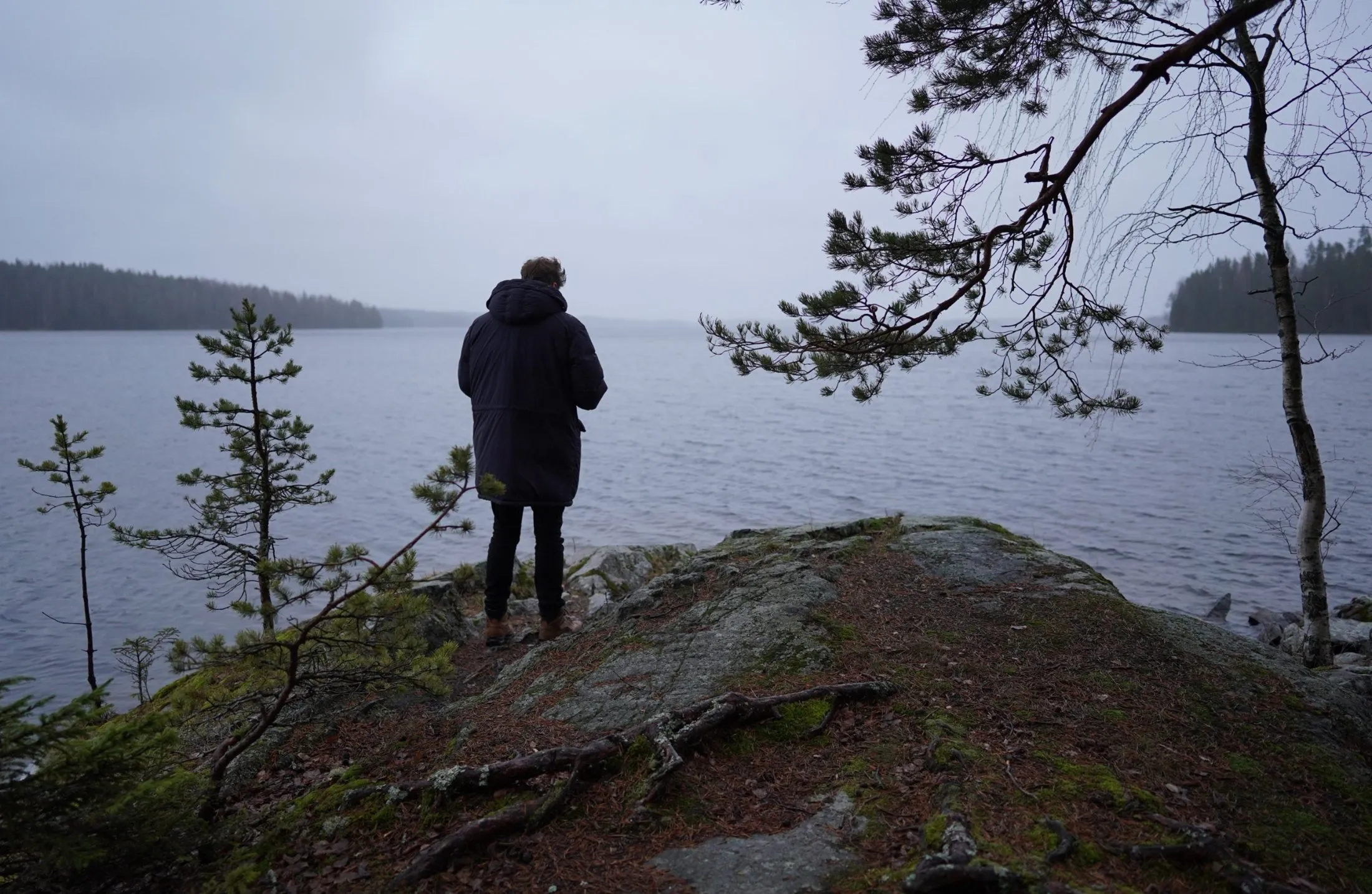 A person standing on a lakeside rock and looking across the water.